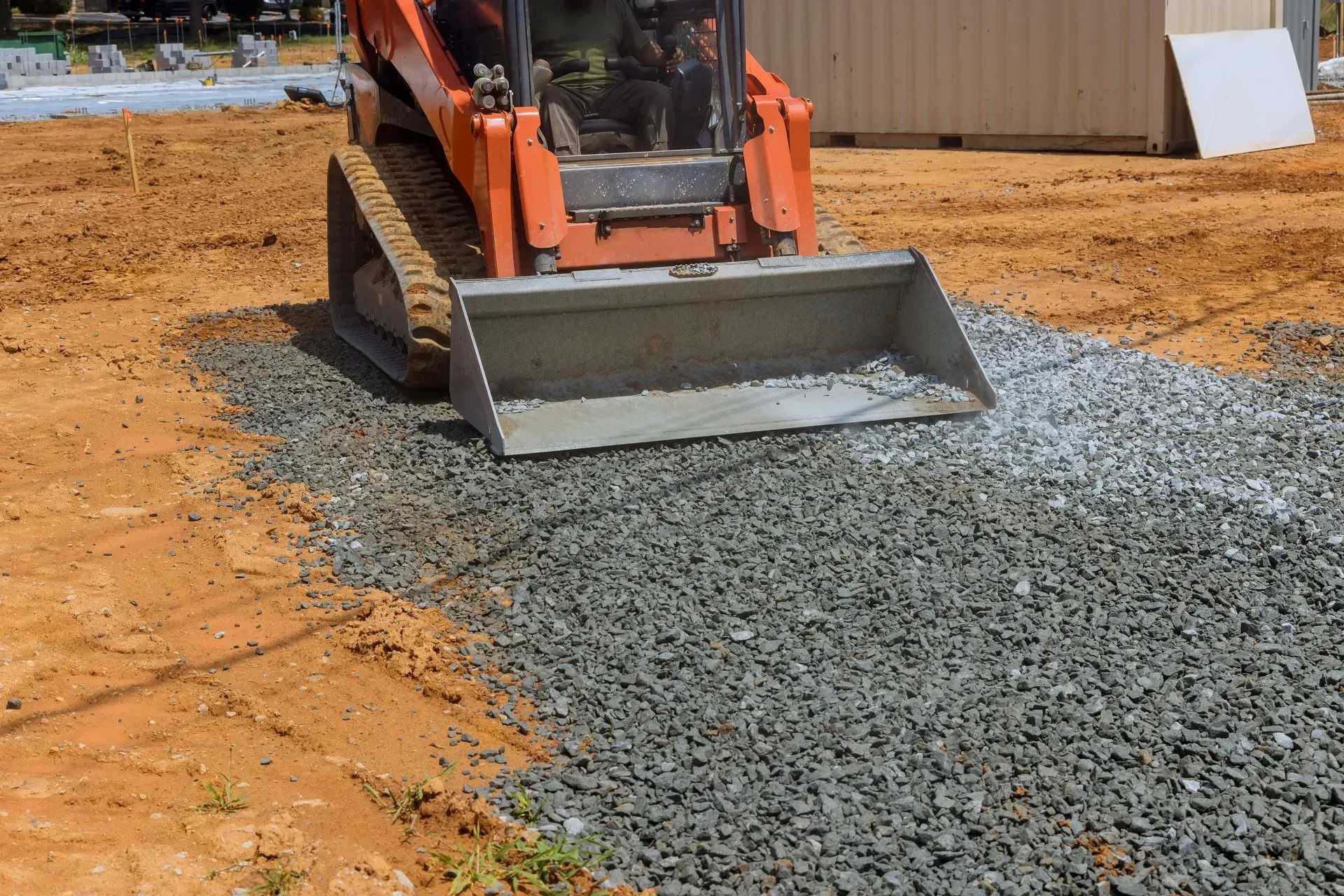 Orange skid steer spreading gray gravel on a dirt construction site