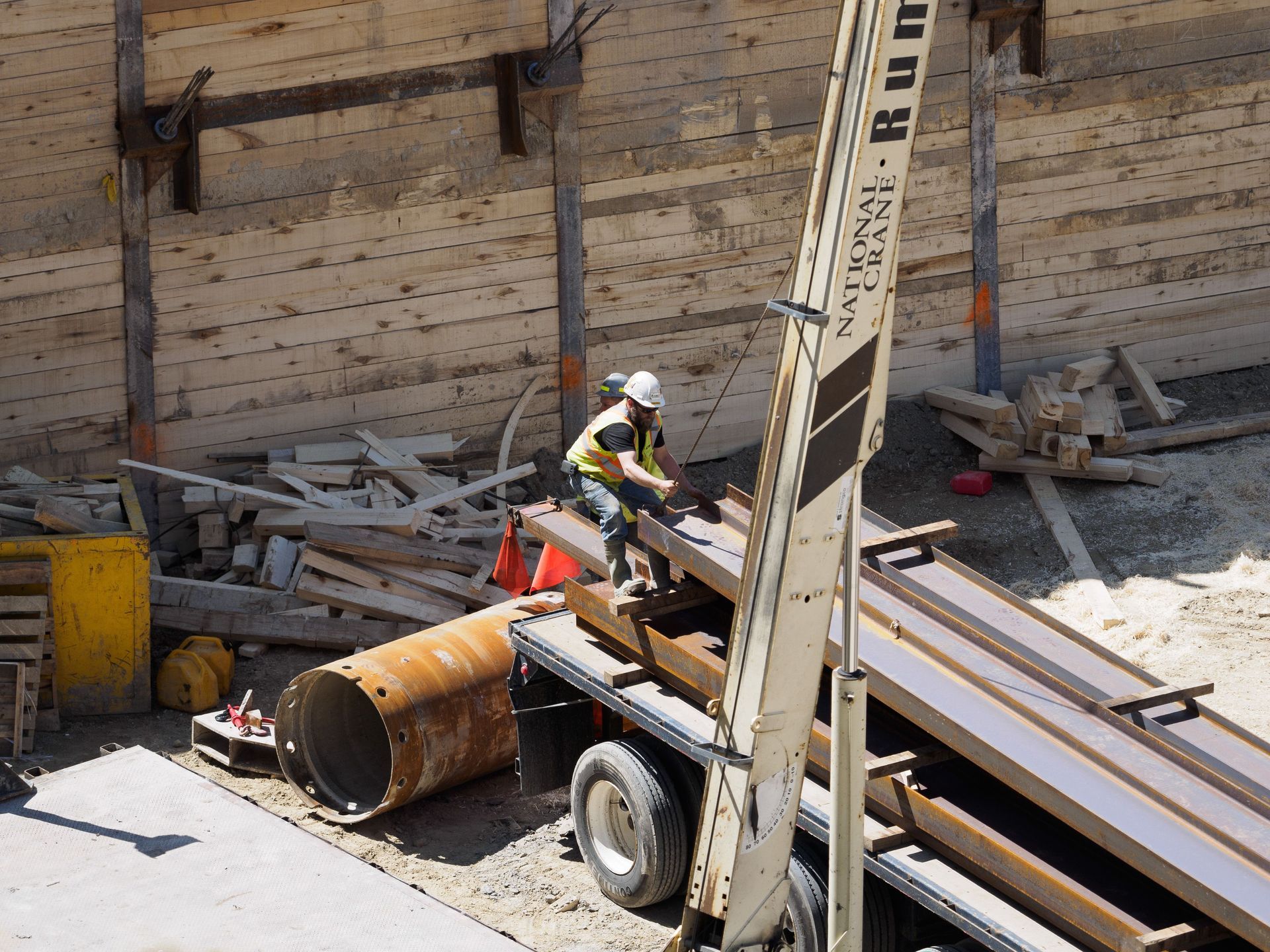 Worker in hard hat operating construction equipment beside lumber and debris at a worksite