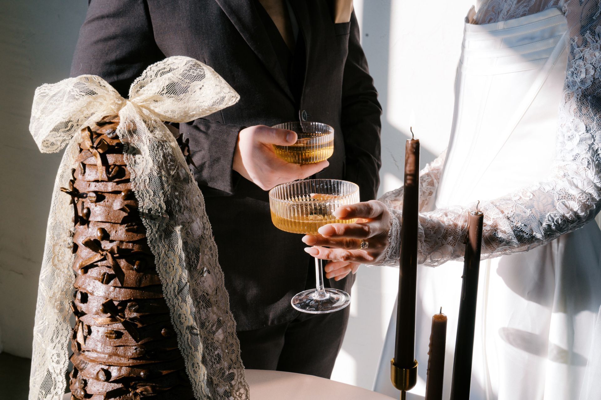 Bride and groom with cocktails next to their chocolate wedding cake at Bestow Events in Longmont, CO.