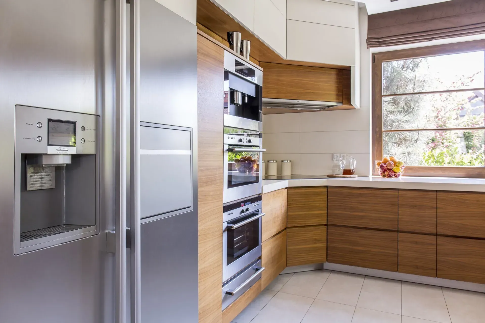 Modern kitchen with stainless steel refrigerator and built-in oven. Wooden cabinetry and window with natural light.