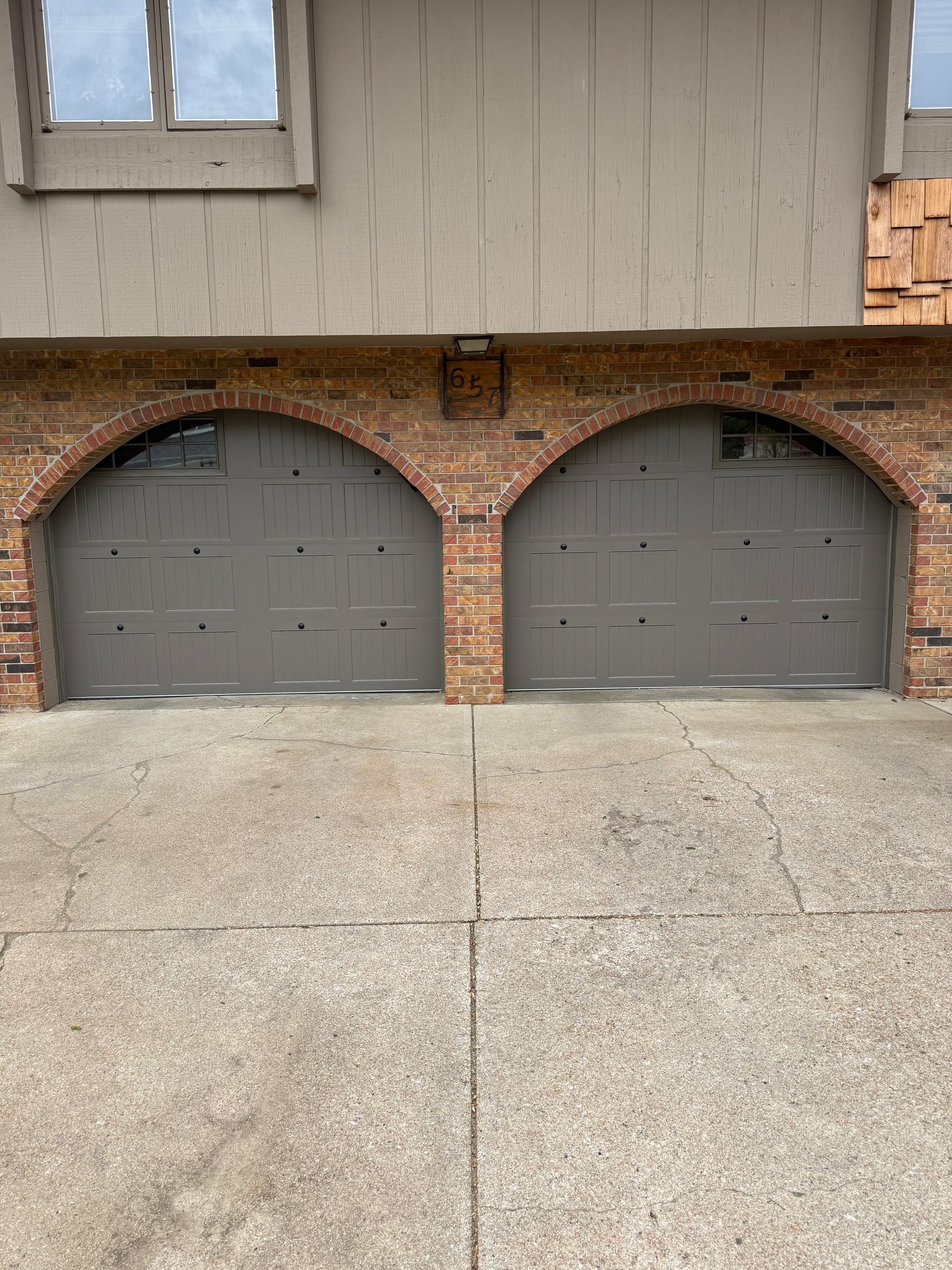 Two gray arched garage doors in a brick facade with a concrete driveway.
