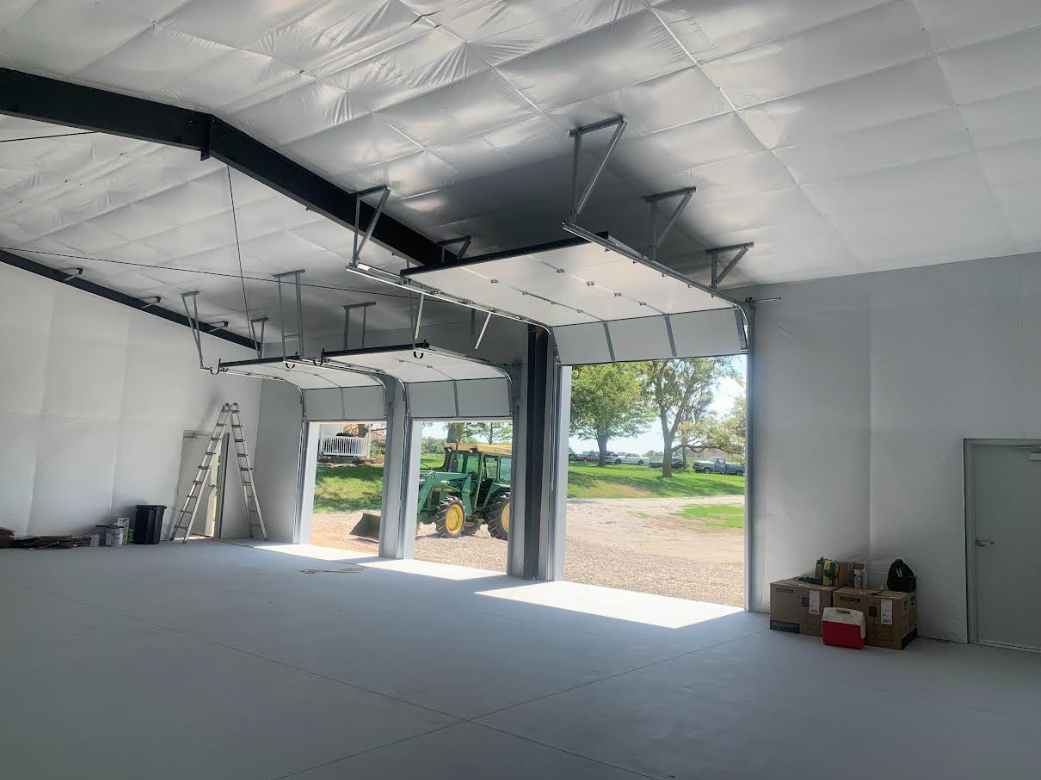 Empty indoor warehouse with open bay doors, white insulated walls, and construction materials on the floor