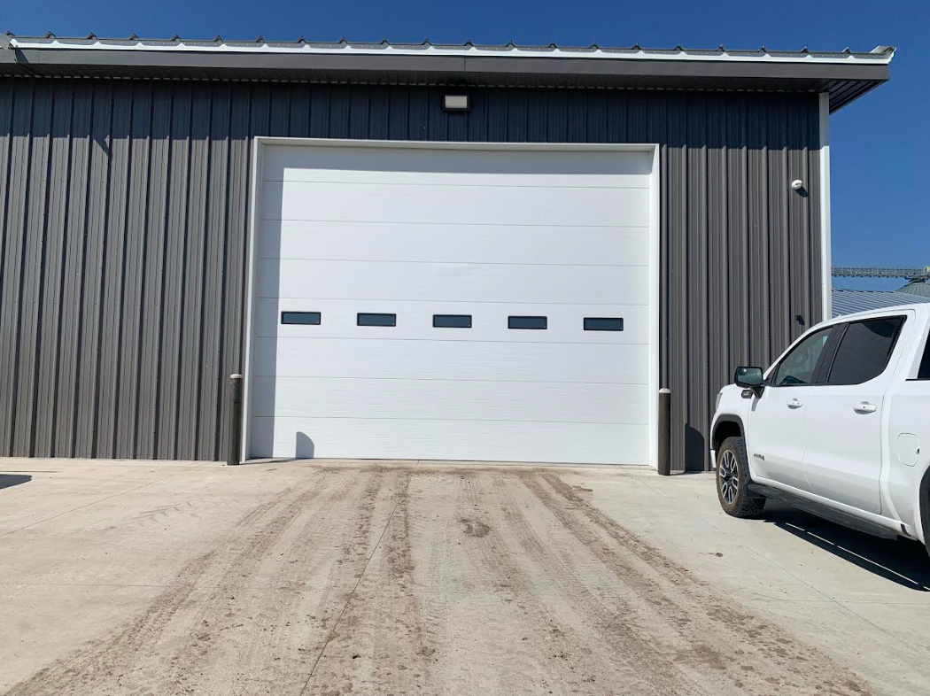 Gray industrial garage with a large white roll-up door and a white pickup truck parked beside it.