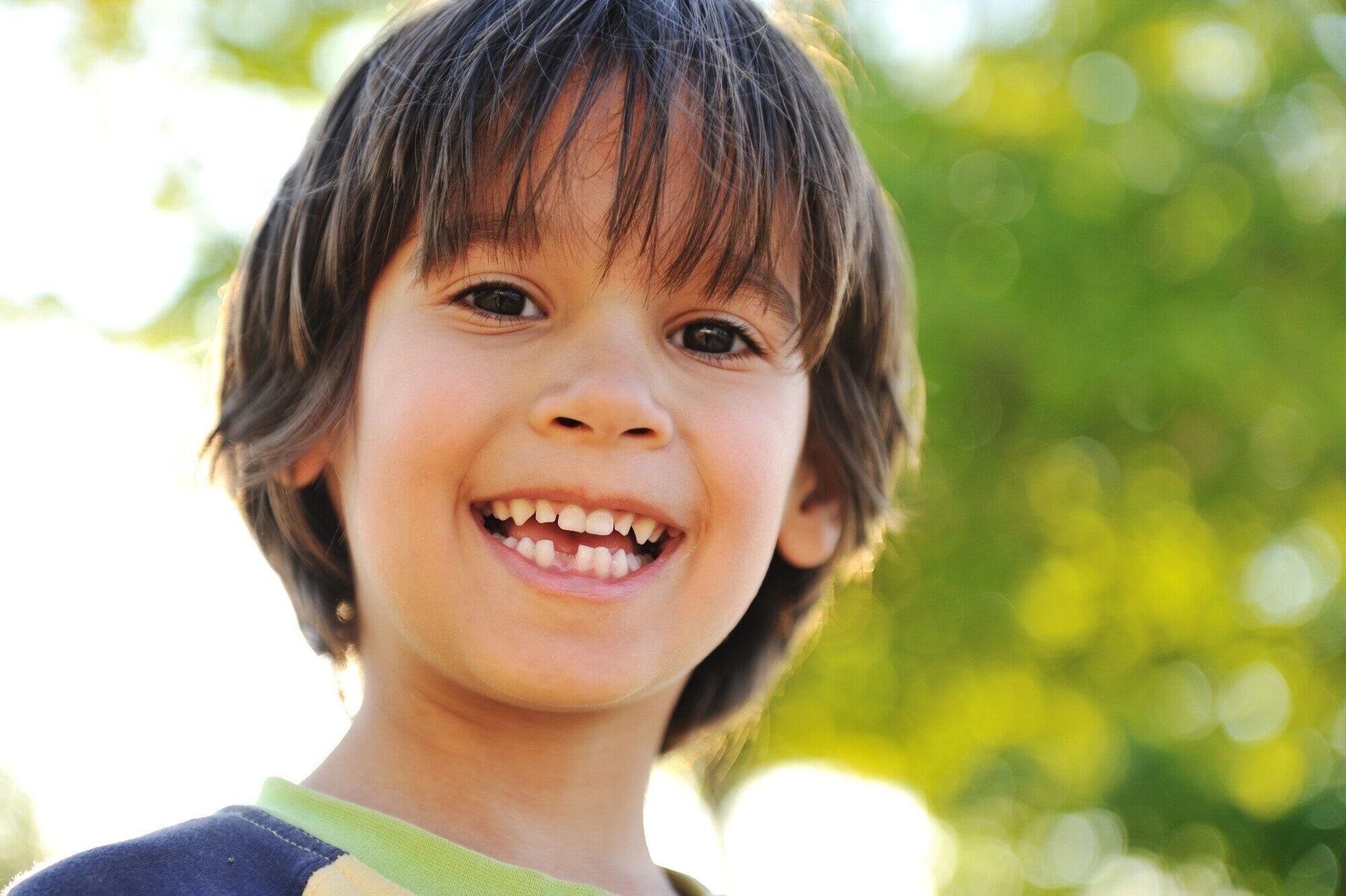 Smiling child with missing front tooth, against a blurred green background.
