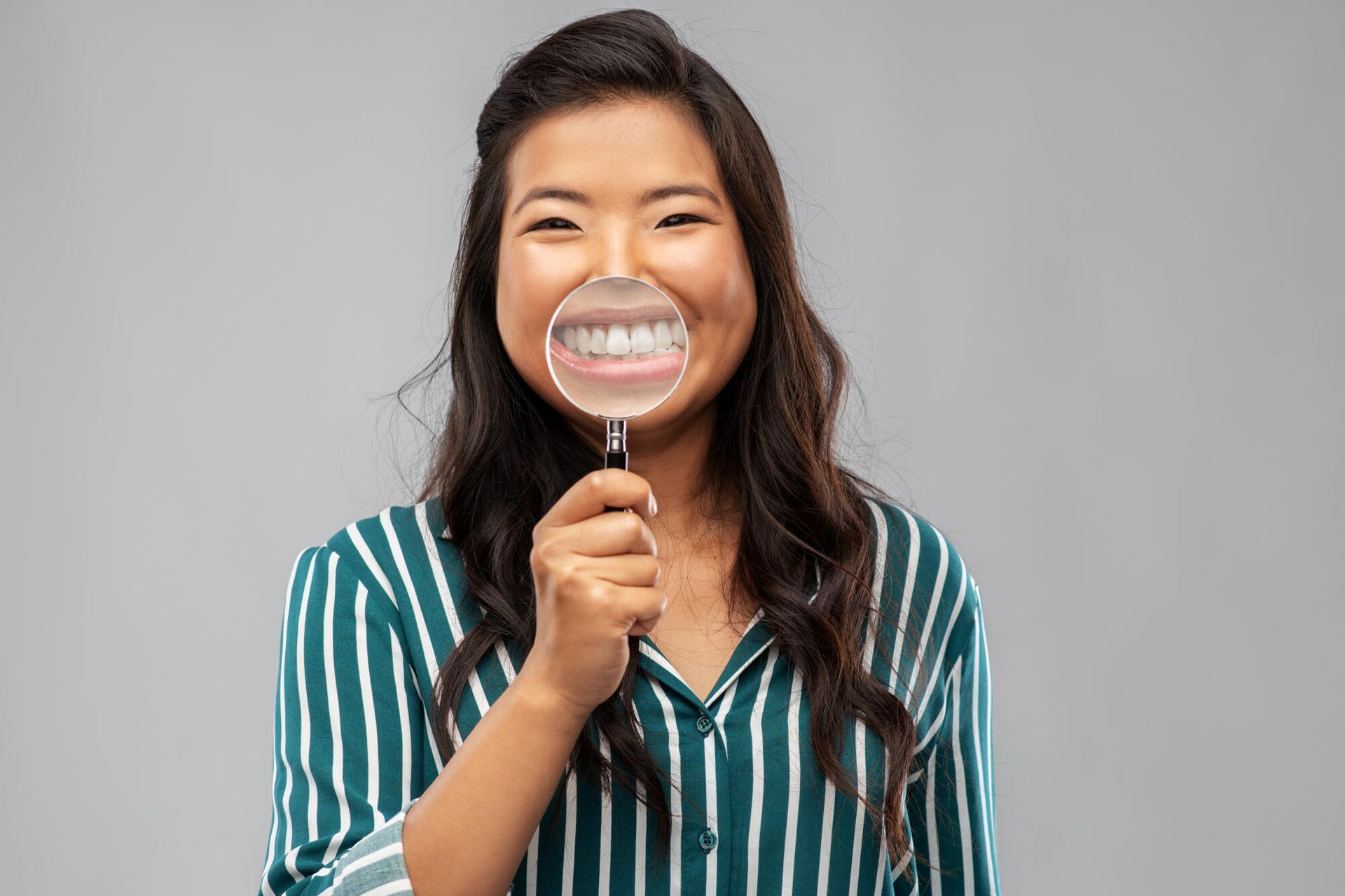 Woman holding a magnifying glass over her smiling mouth, showing teeth.