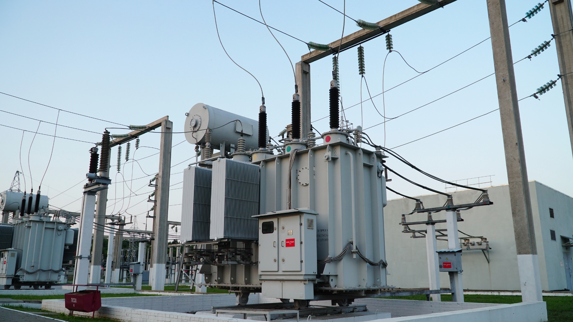 A large transformer is sitting in a power station next to a building.