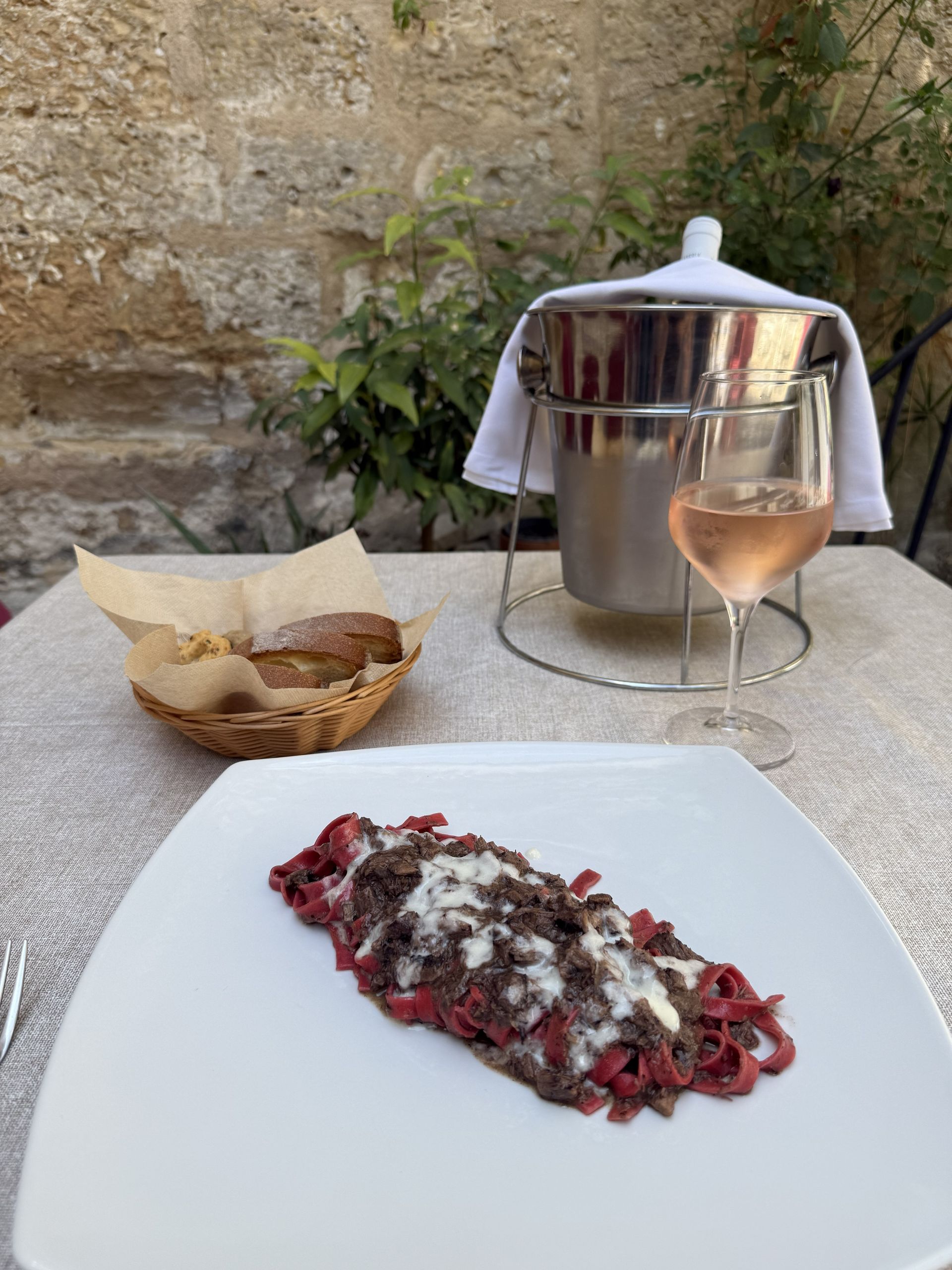 Pasta rossa con panna servita su un tavolo da patio, accanto a pane, un bicchiere di vino e un refrigeratore.