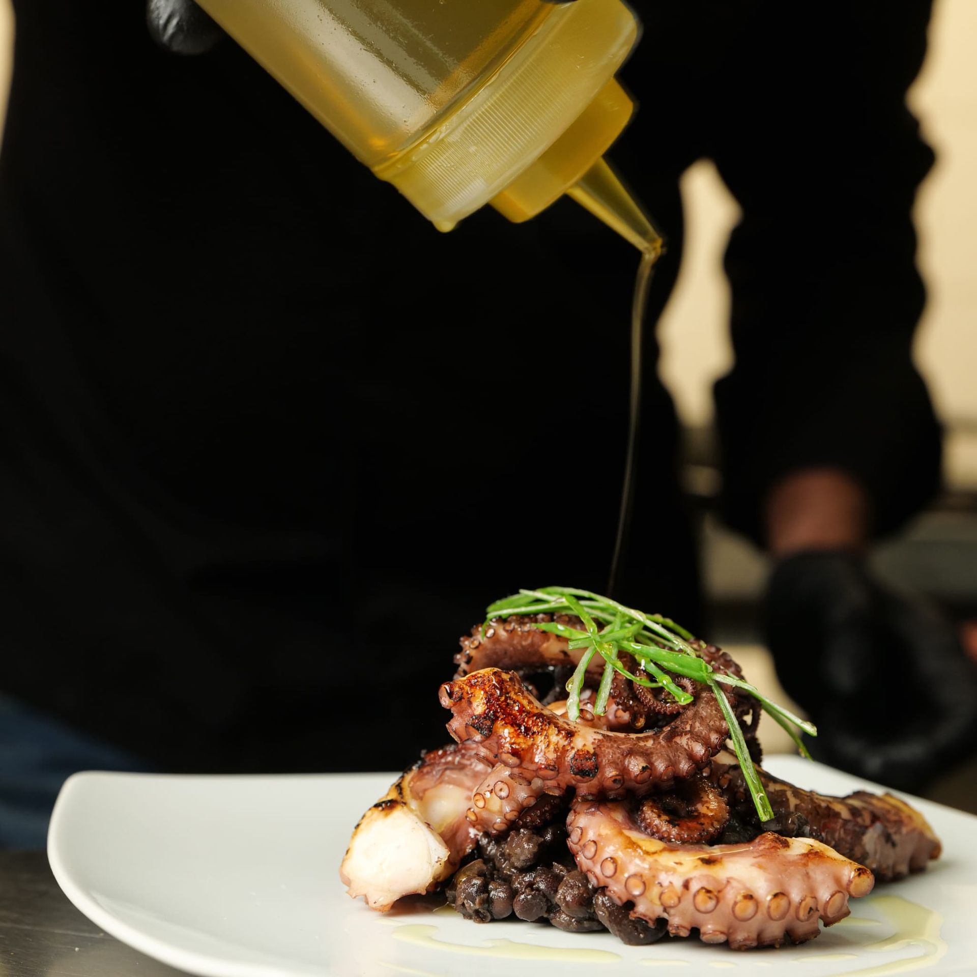 Piatto di polpo su un piatto bianco, irrorato di salsa e guarnito con erbe aromatiche.