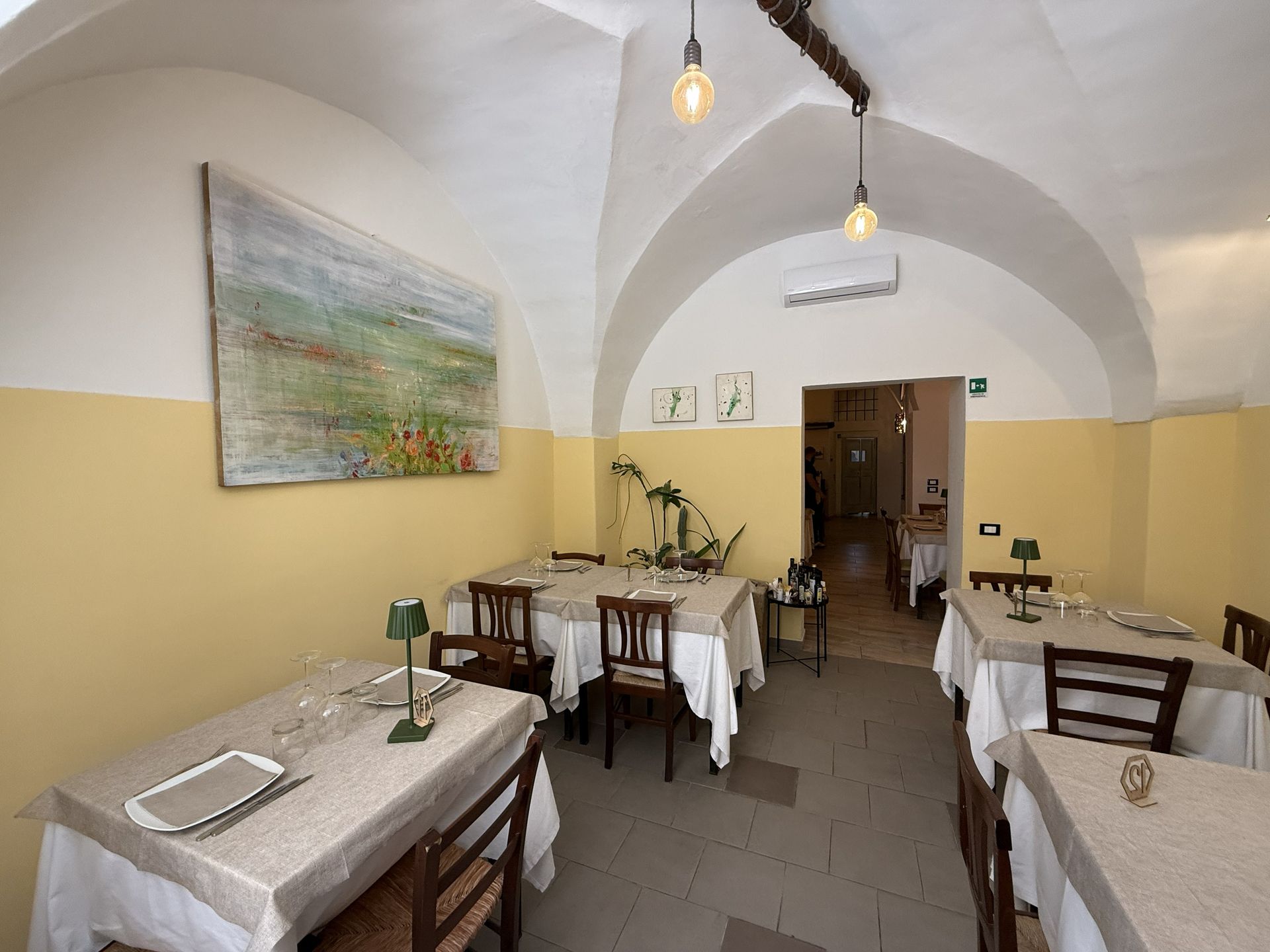 Accogliente sala da pranzo di un ristorante con soffitti a volta, tovaglie bianche e calde lampade a sospensione.