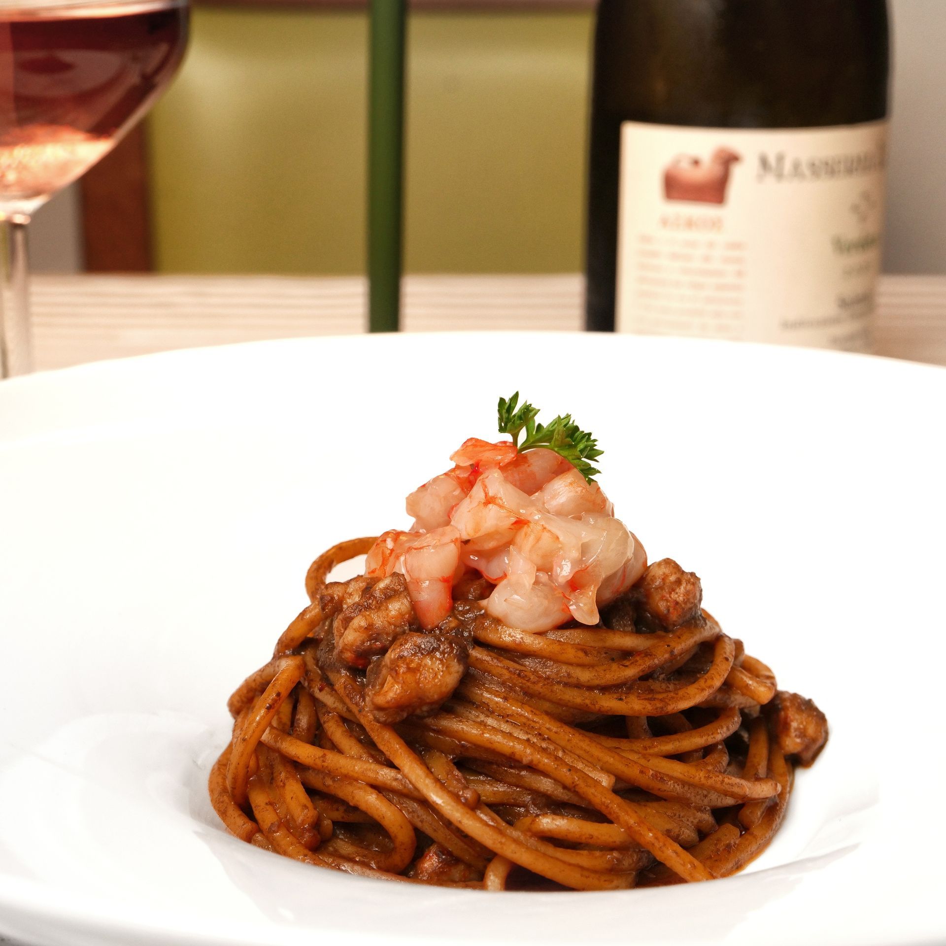 Nido di spaghetti guarnito con frutti di mare a dadini e prezzemolo su un piatto bianco in un ambiente da ristorante.