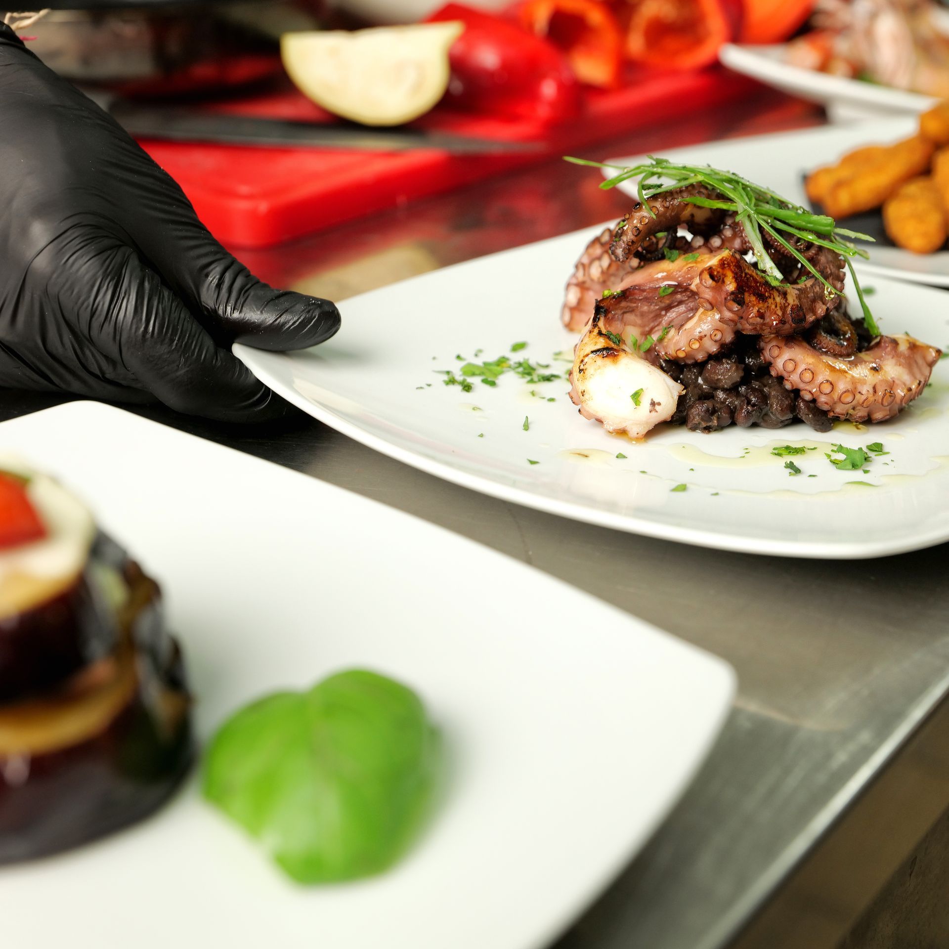 In cucina, uno chef impiatta il polpo su un piatto bianco con una mano guantata di nero.