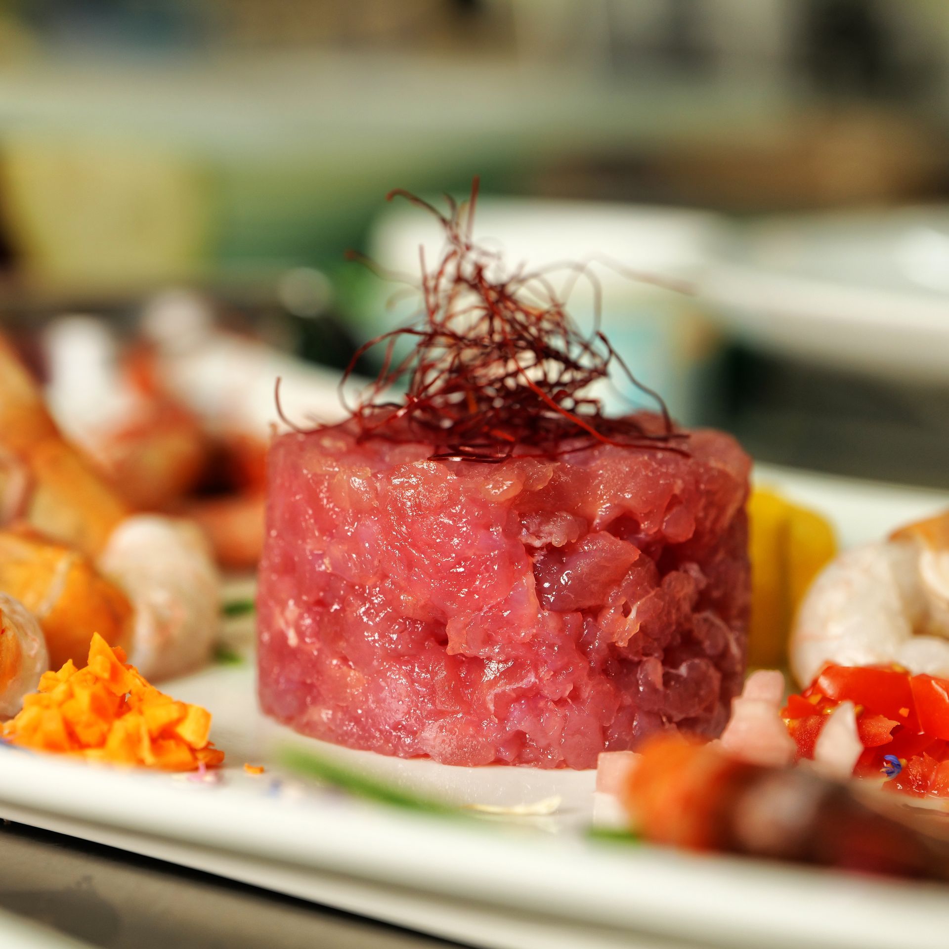 Tartelletta di tartare di tonno rosa guarnita con fili sottili, servita su un piatto bianco con decorazioni.
