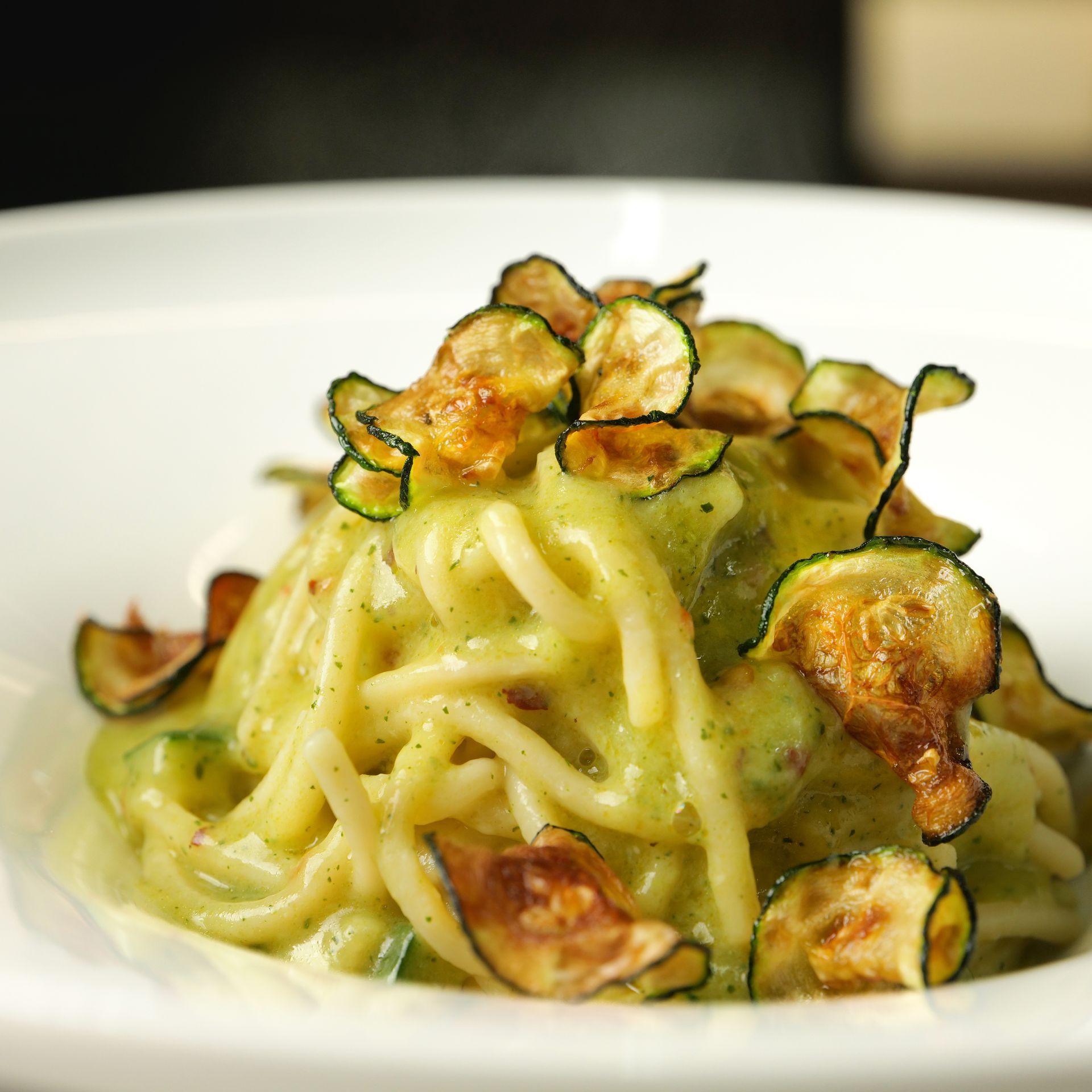 Spaghetti in salsa verde cremosa con chips di zucchine croccanti in una ciotola bianca