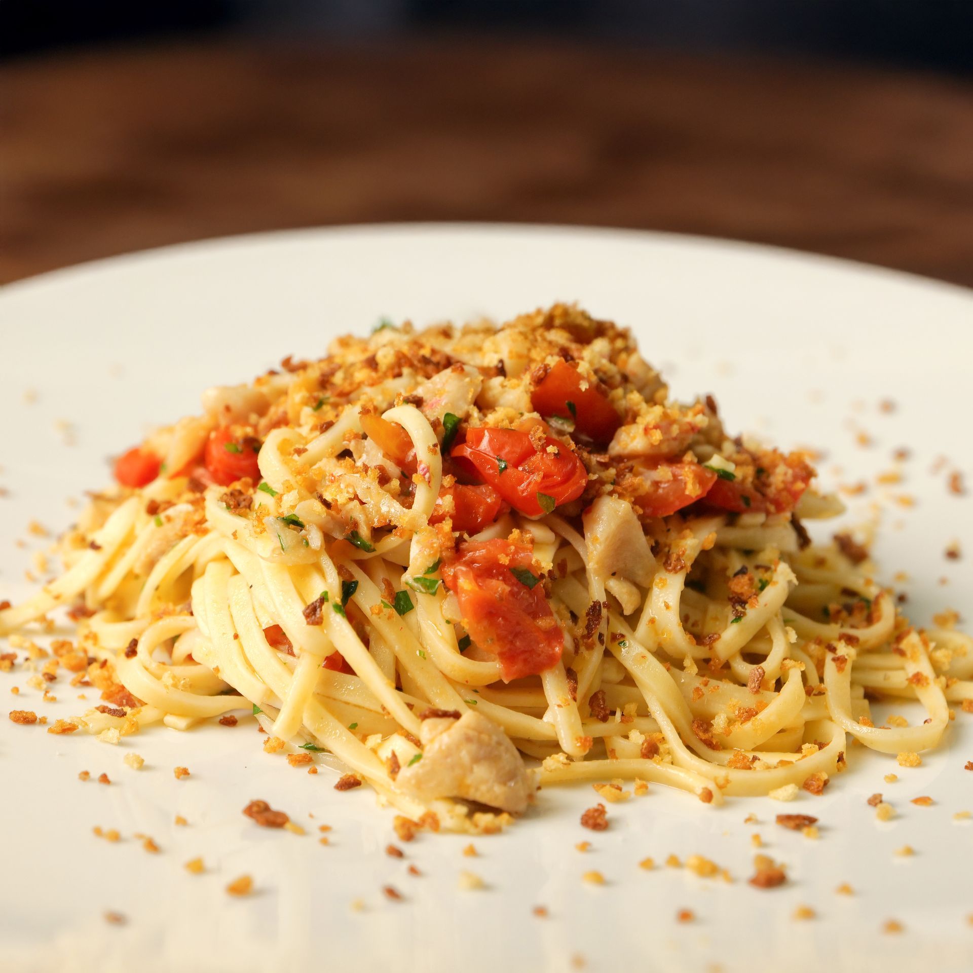 Spaghetti impiattati con salsa di pomodoro, formaggio grattugiato e pangrattato su un piatto bianco.