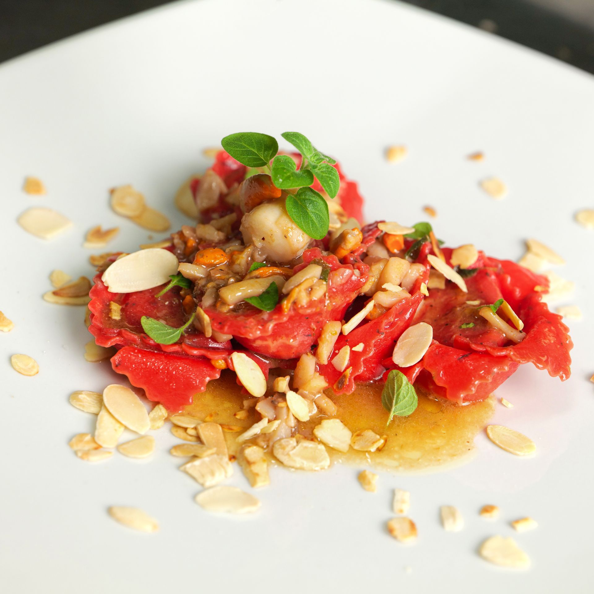 Insalata di pomodori con scaglie di mandorle ed erbe aromatiche fresche su un piatto bianco.