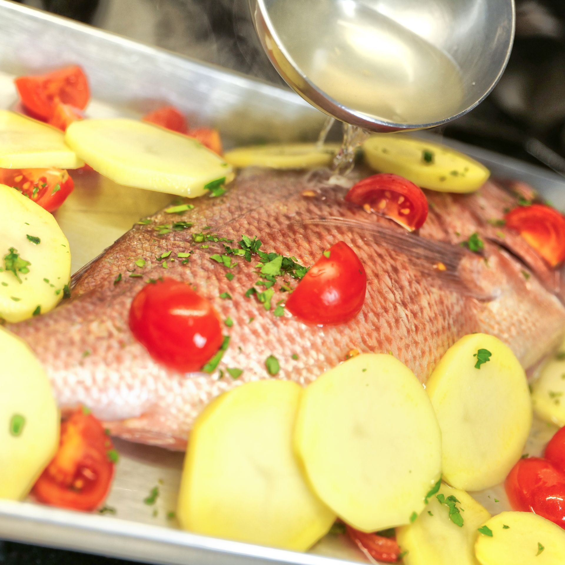 Pesce intero al forno con patate, pomodori ed erbe aromatiche in una teglia