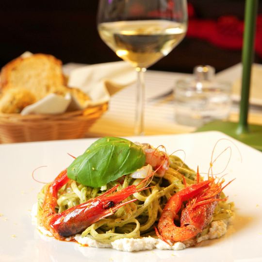 Pasta con gamberi rossi e basilico su un piatto bianco, con un bicchiere di vino bianco sullo sfondo.