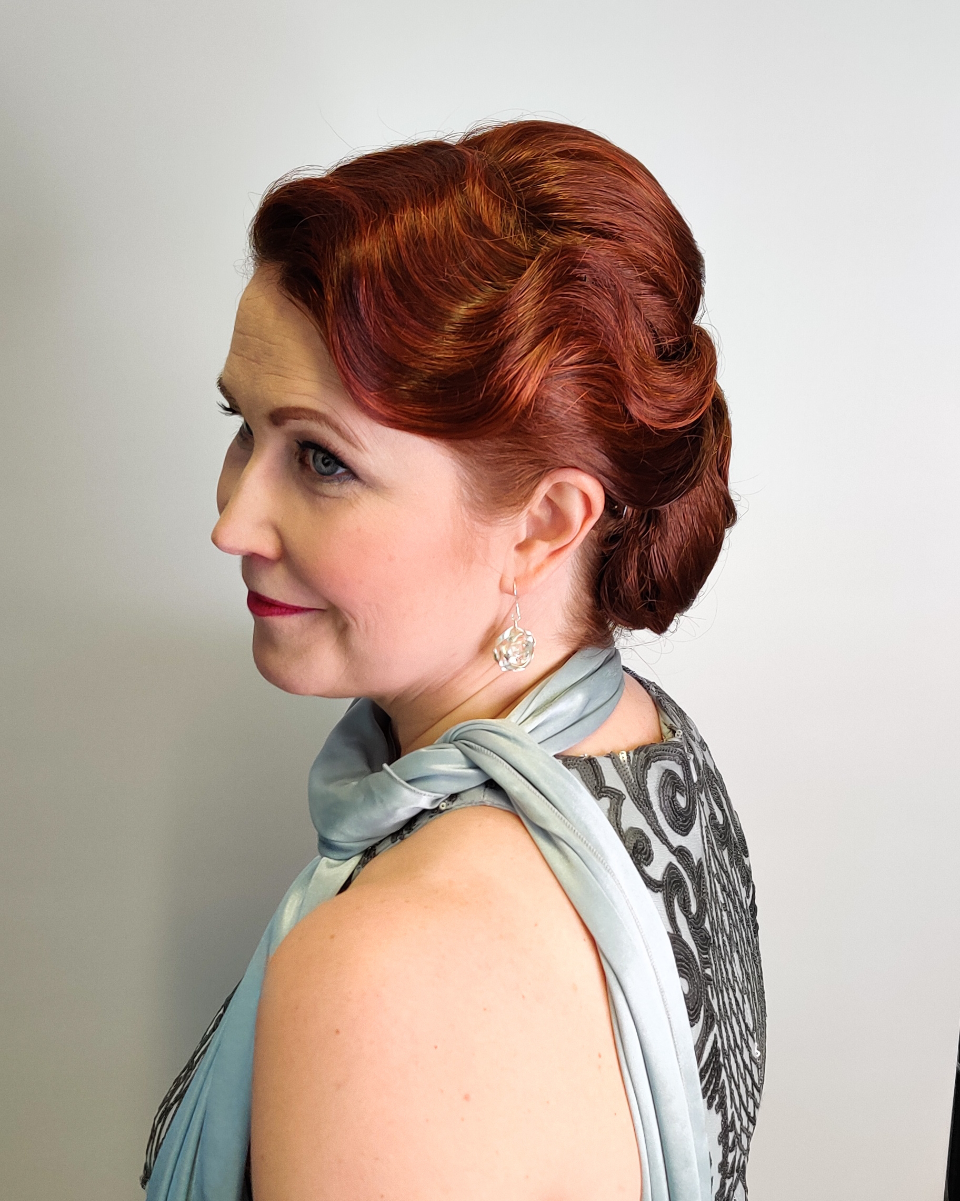 A woman with red hair is wearing a blue dress and a scarf around her neck.