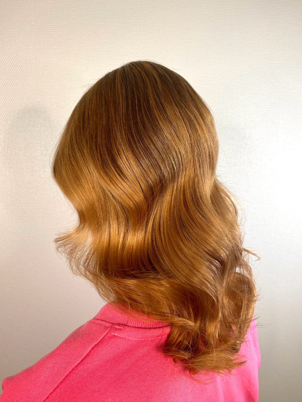 The woman is wearing a pink sweater and has long wavy hair.