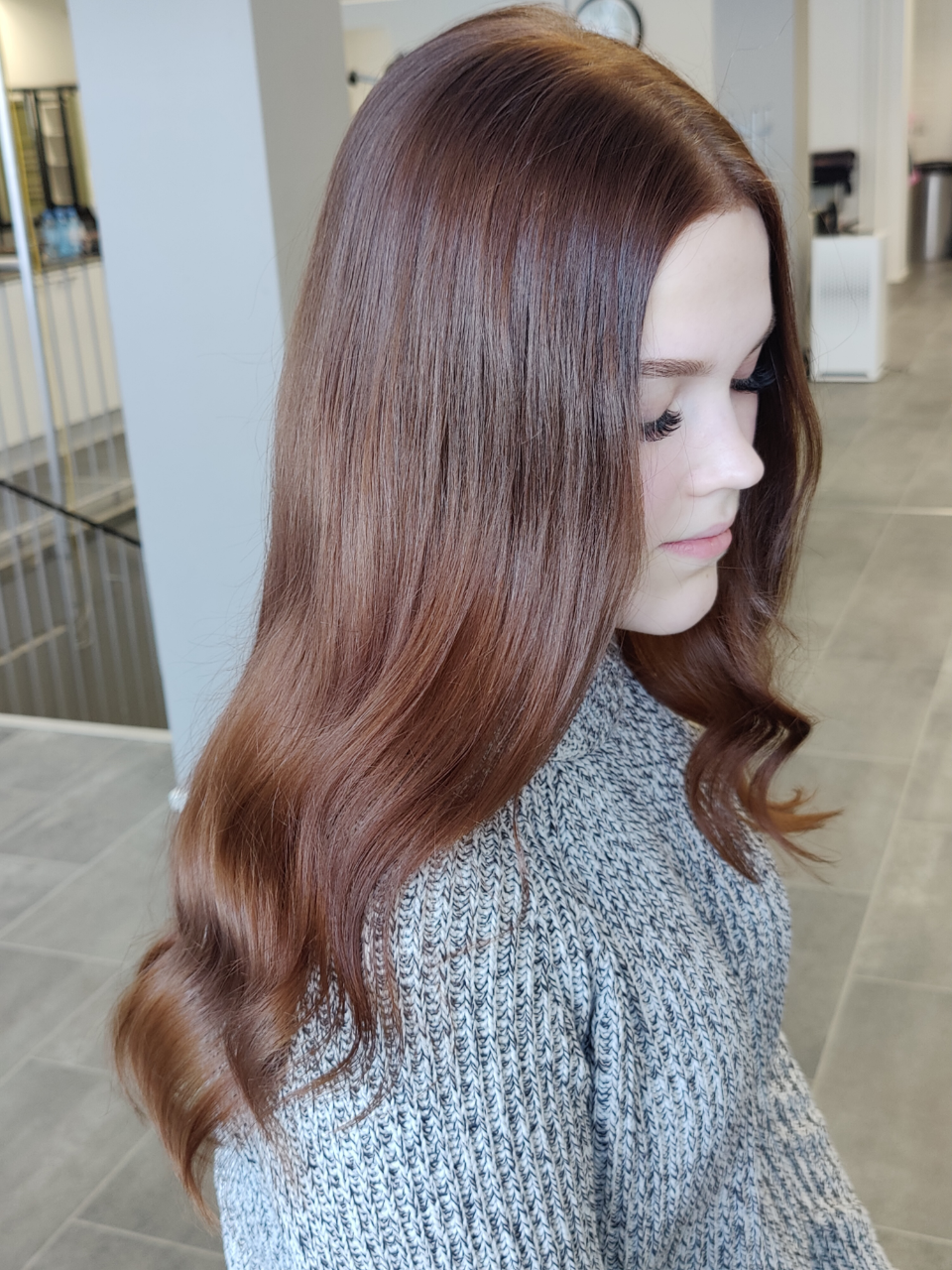 A woman with long brown hair is wearing a grey sweater.