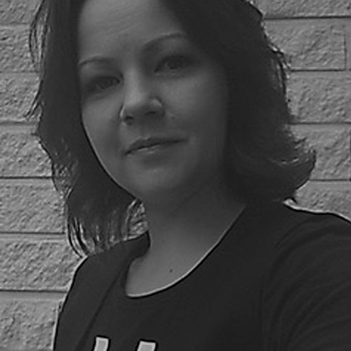 A black and white photo of a woman standing in front of a brick wall.