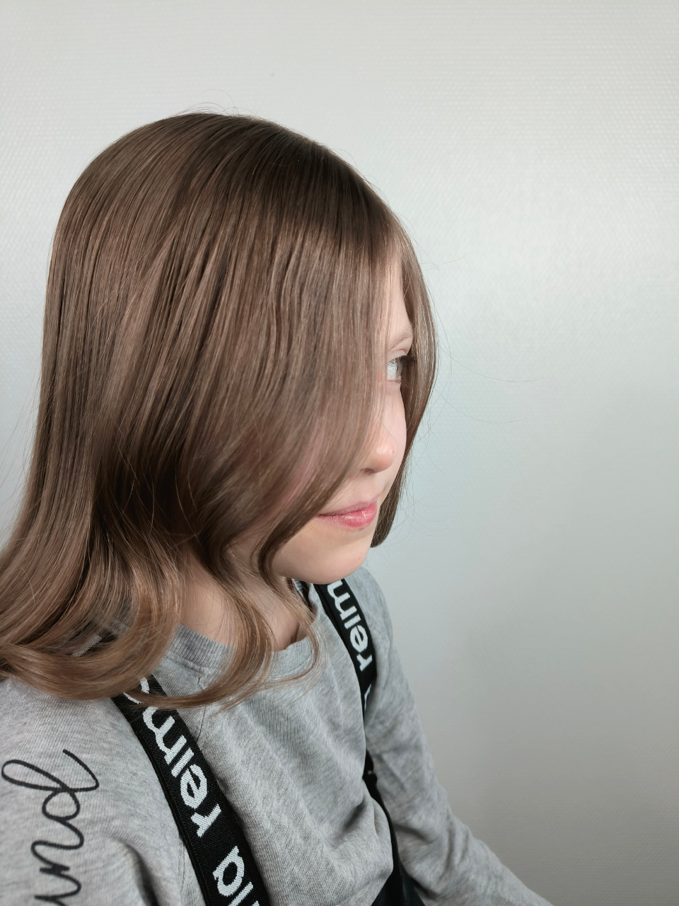 A young girl with long brown hair is wearing a gray sweater and black suspenders.