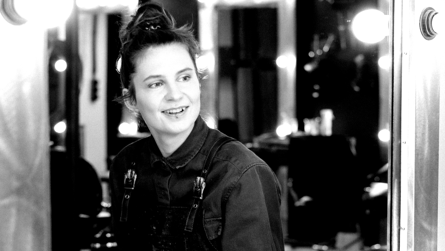 A woman is smiling in front of a mirror in a black and white photo.