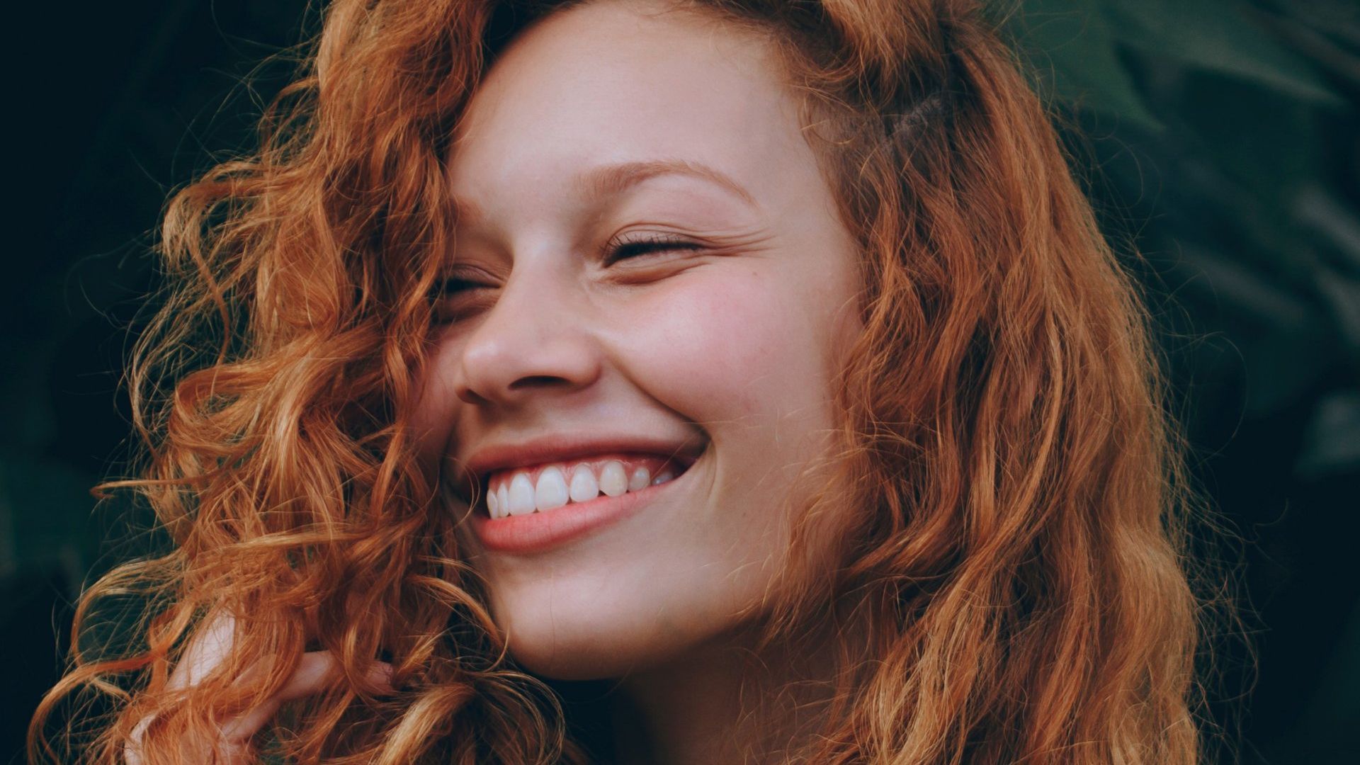 A close up of a woman with red hair smiling.