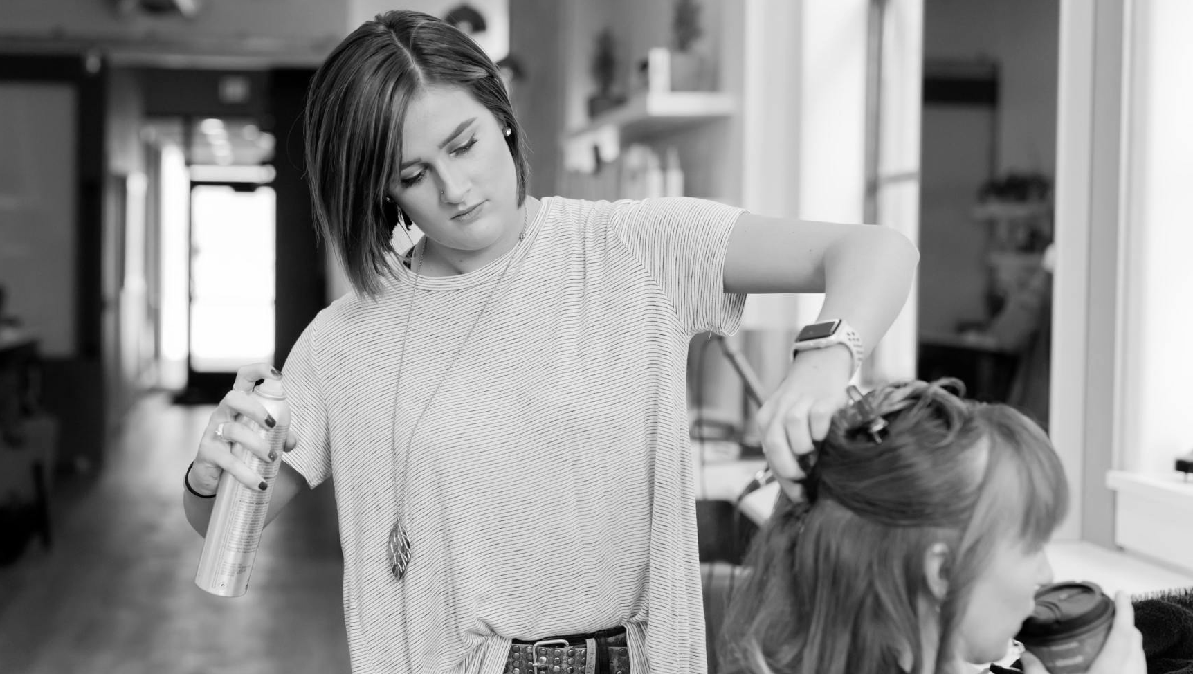 A woman is spraying a woman 's hair in a black and white photo.
