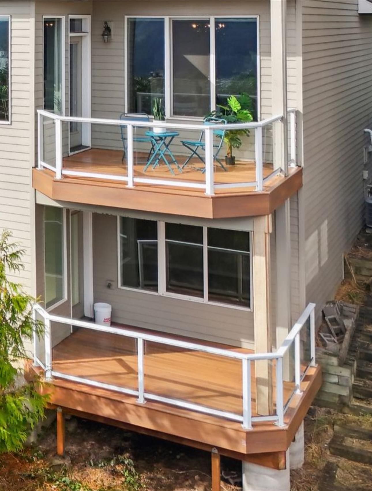A two-story house exterior featuring two stacked, wood-toned balconies with white railings and seating on the top deck.