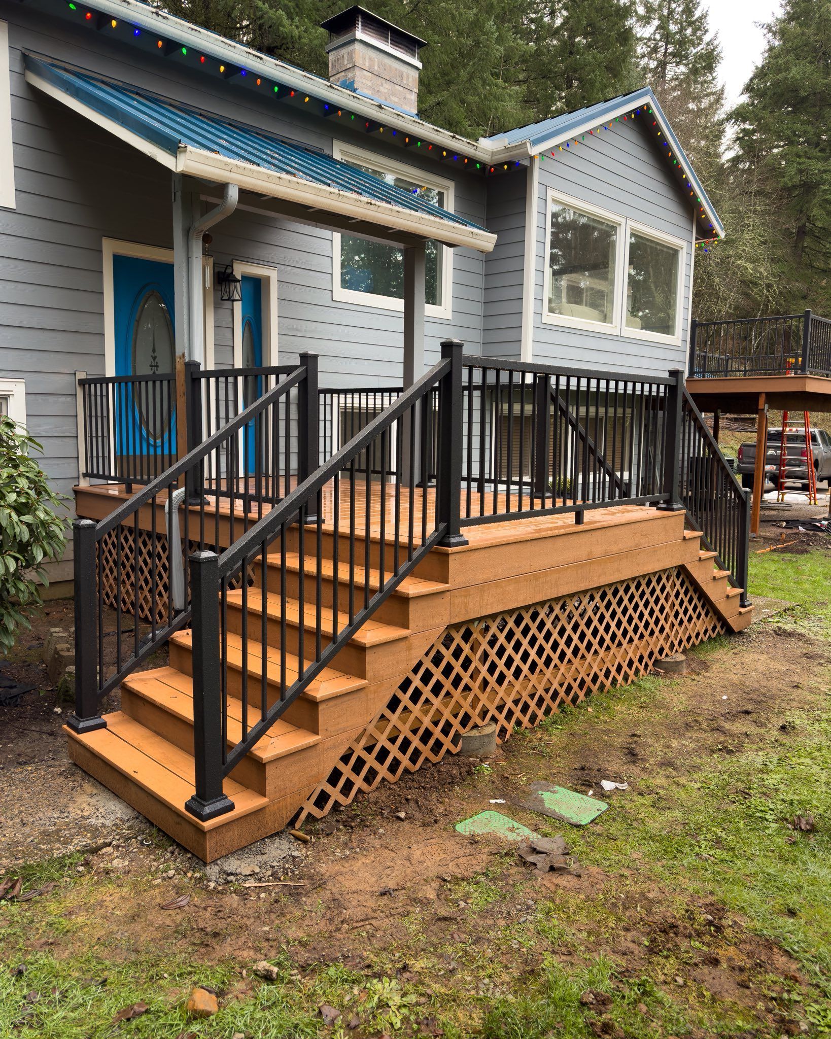 A house exterior featuring a newly built brown wooden deck and stairs with black railings, set against a grey-sided home.