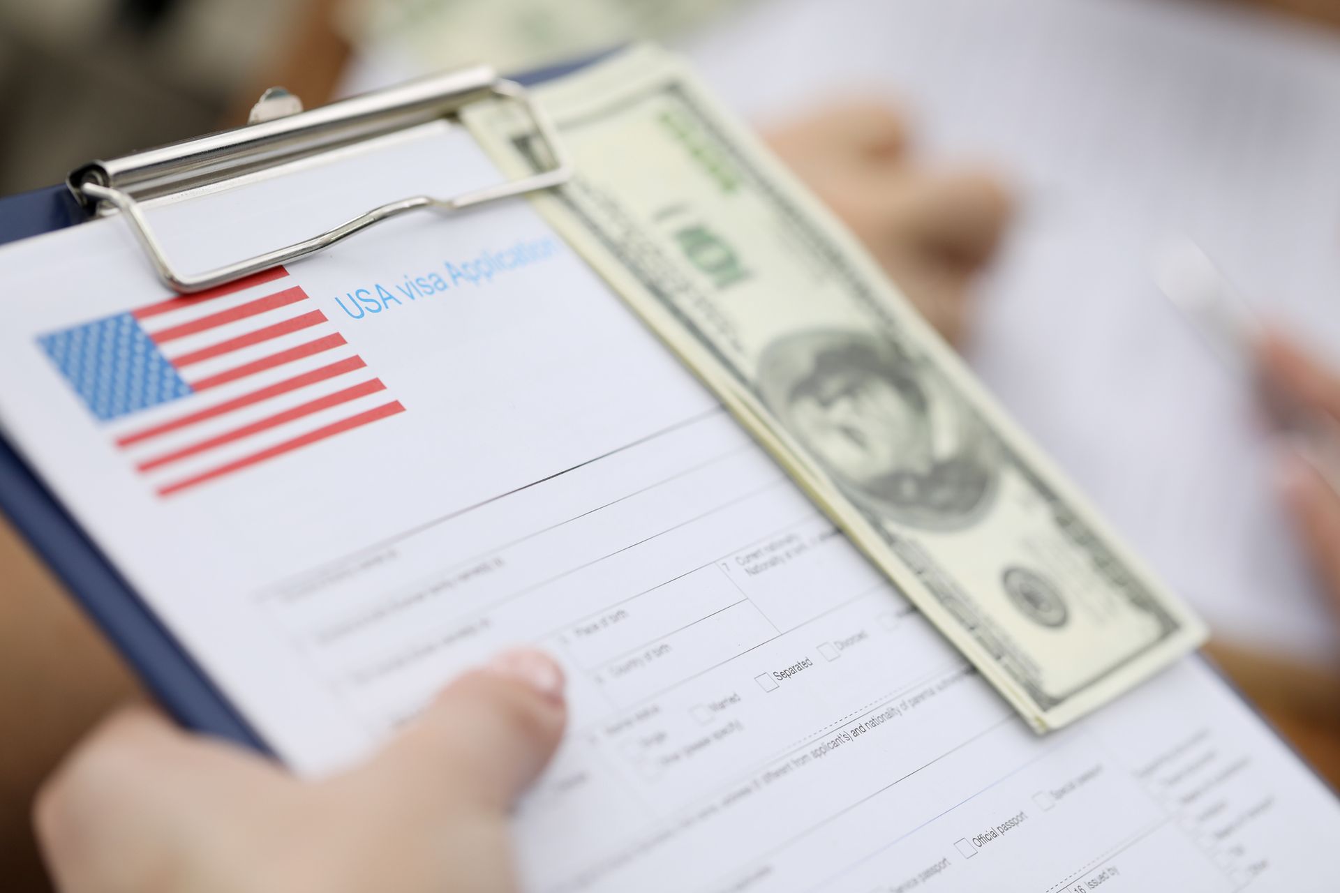 Portapapeles con una solicitud de visa de EE. UU., dinero en efectivo y manos.