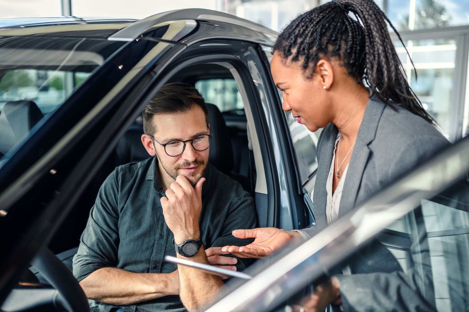 A car salesperson showing a man a vehicle's interior. They are in a car dealership. A car salesperson showing a man a vehicle's interior. They are in a car dealership.