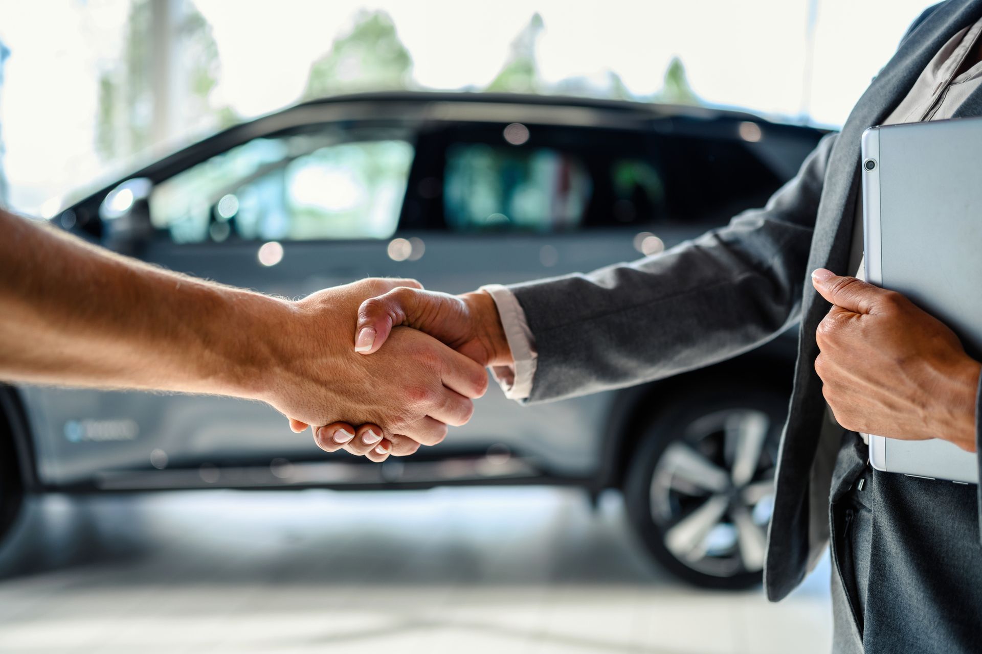 Apretón de manos entre un cliente y un vendedor de automóviles en un concesionario de automóviles, con un automóvil visible en el fondo.