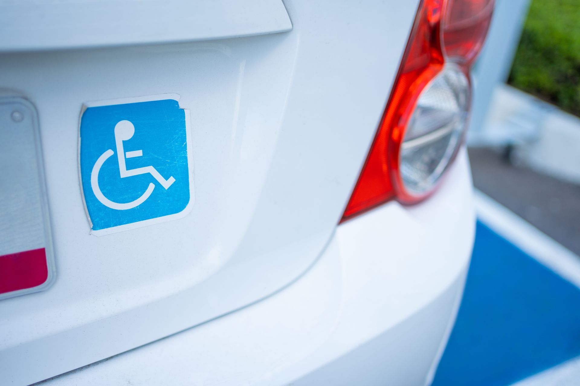 Automóvil blanco con una calcomanía azul de estacionamiento para discapacitados en el maletero cerca de la luz trasera.