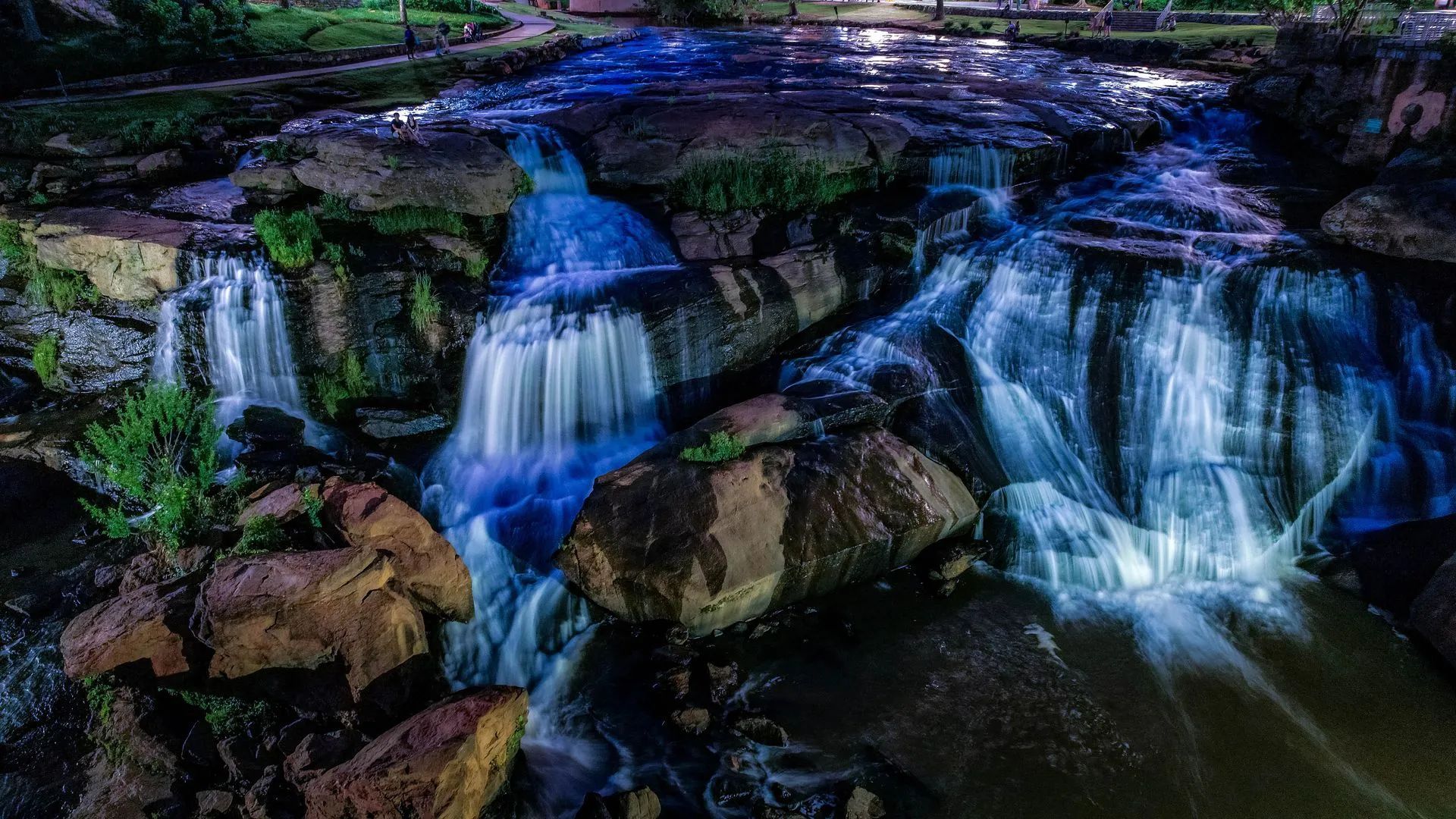 Water cascading over mossy rocks into a dark pool at dusk, with blue-purple reflections.
