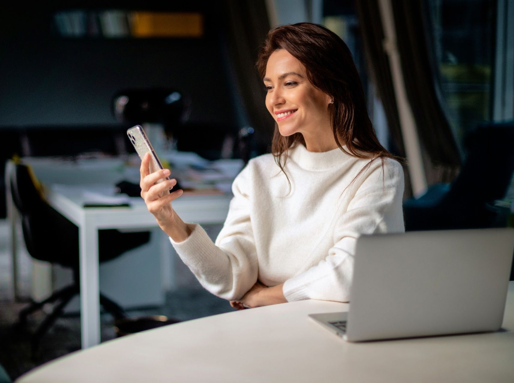 brunette woman 30s in white sweater texting on smartphone
