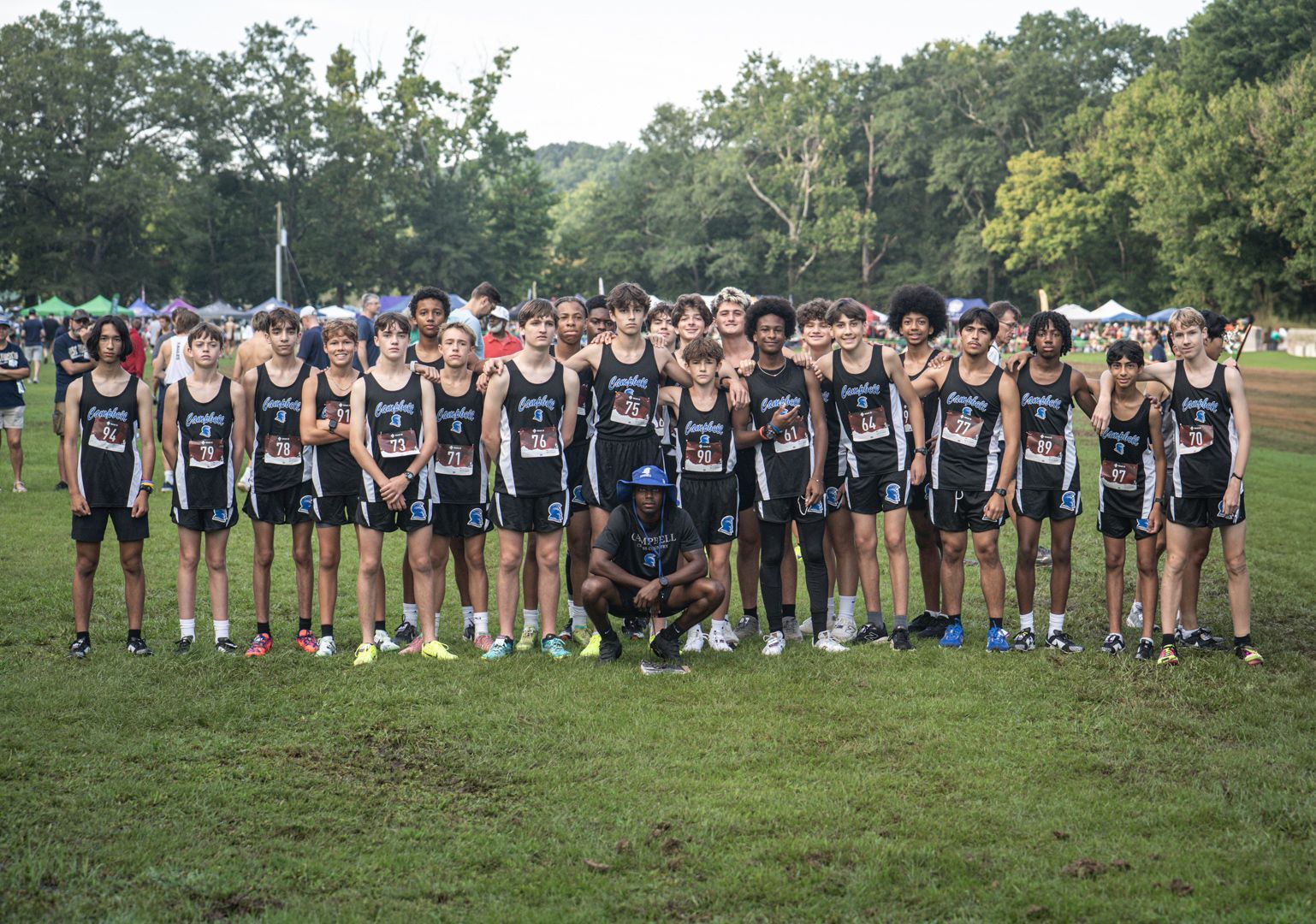 Group of athletes in black uniforms posing on a grassy field with trees in the background