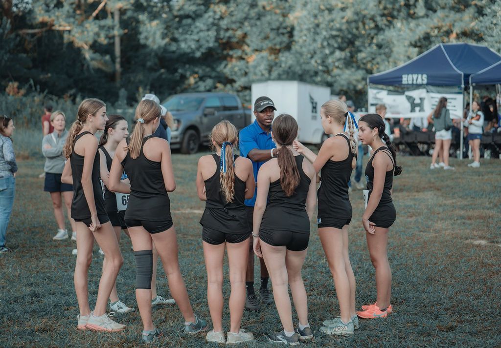 Group of runners in black athletic wear huddled on a grassy field near tents before a race