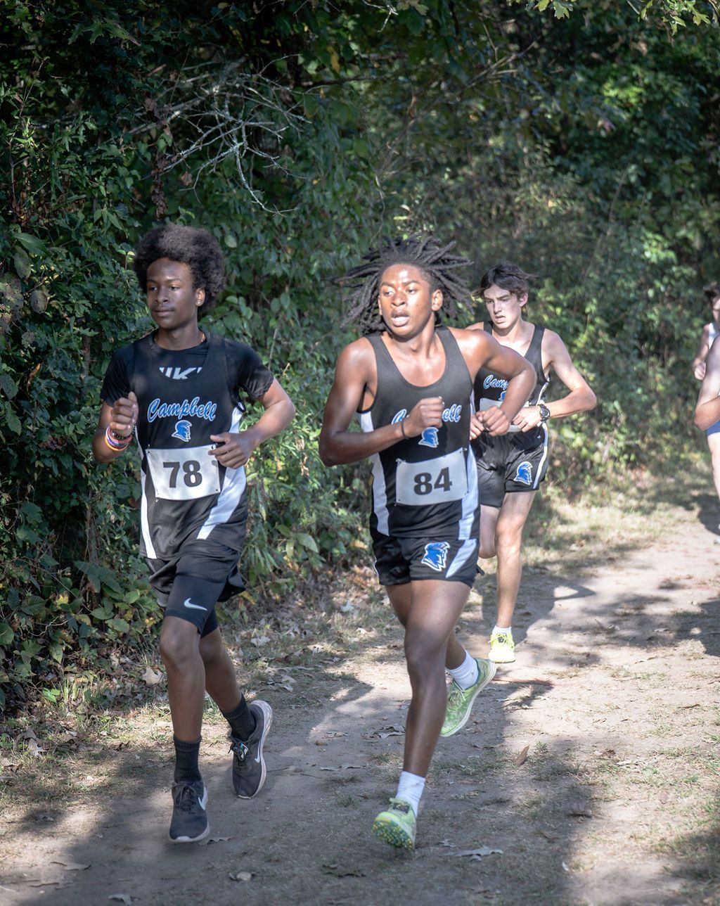 Trail runners wearing bibs race on a wooded dirt path.