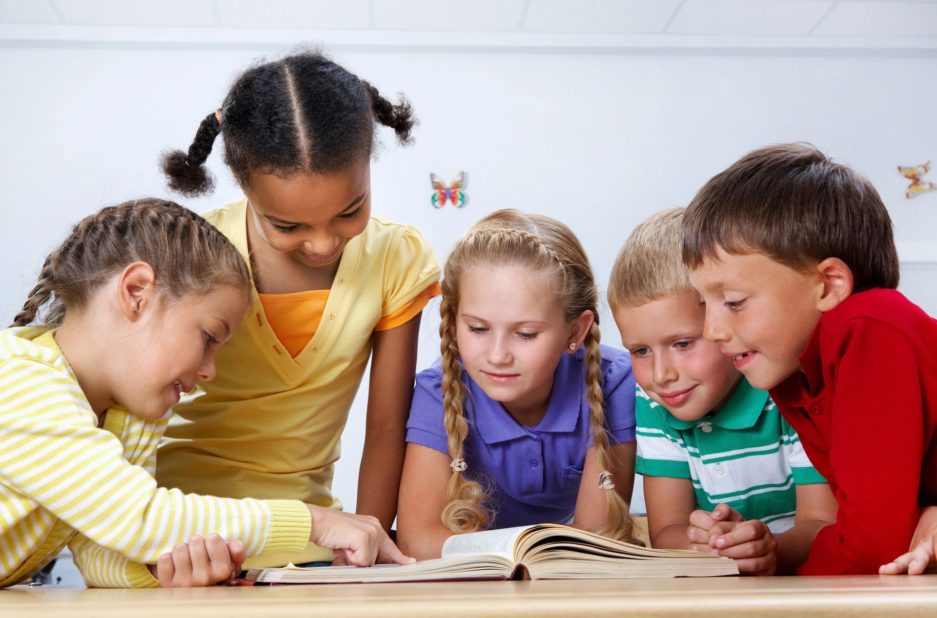 Cinque bambini guardano insieme un libro, probabilmente leggendo in classe.
