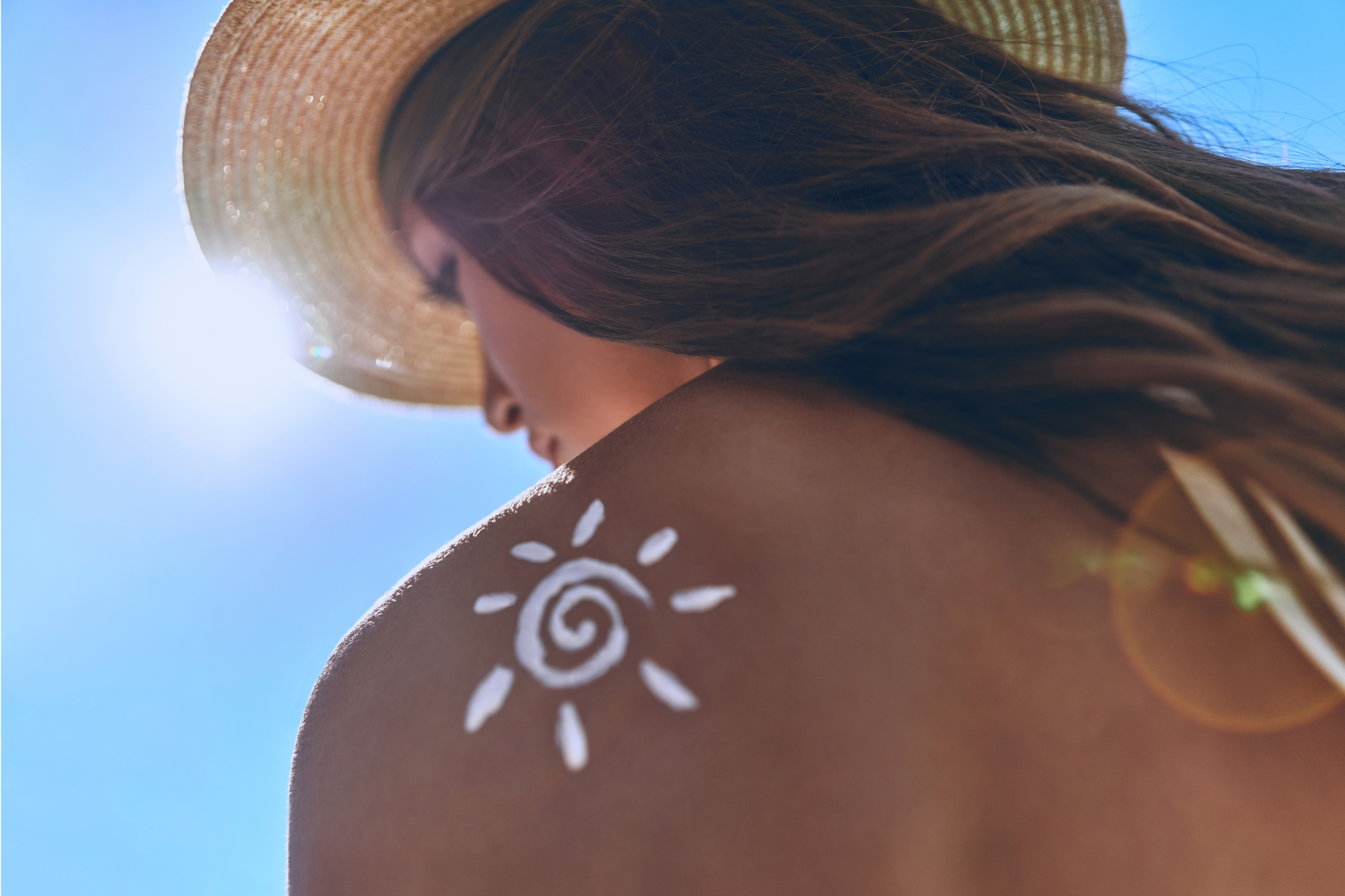 Donna con cappello da sole, crema solare a forma di sole sulla spalla, cielo azzurro brillante.