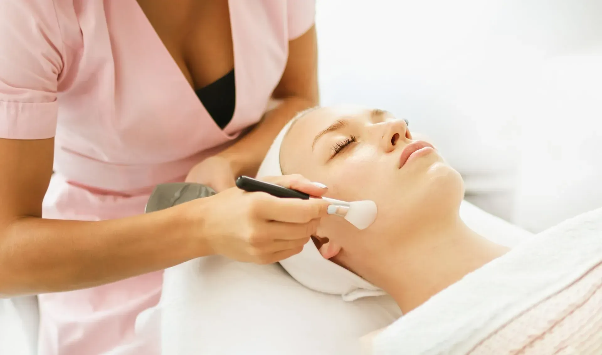 Donna che riceve un trattamento viso in una spa; l'estetista applica il prodotto.