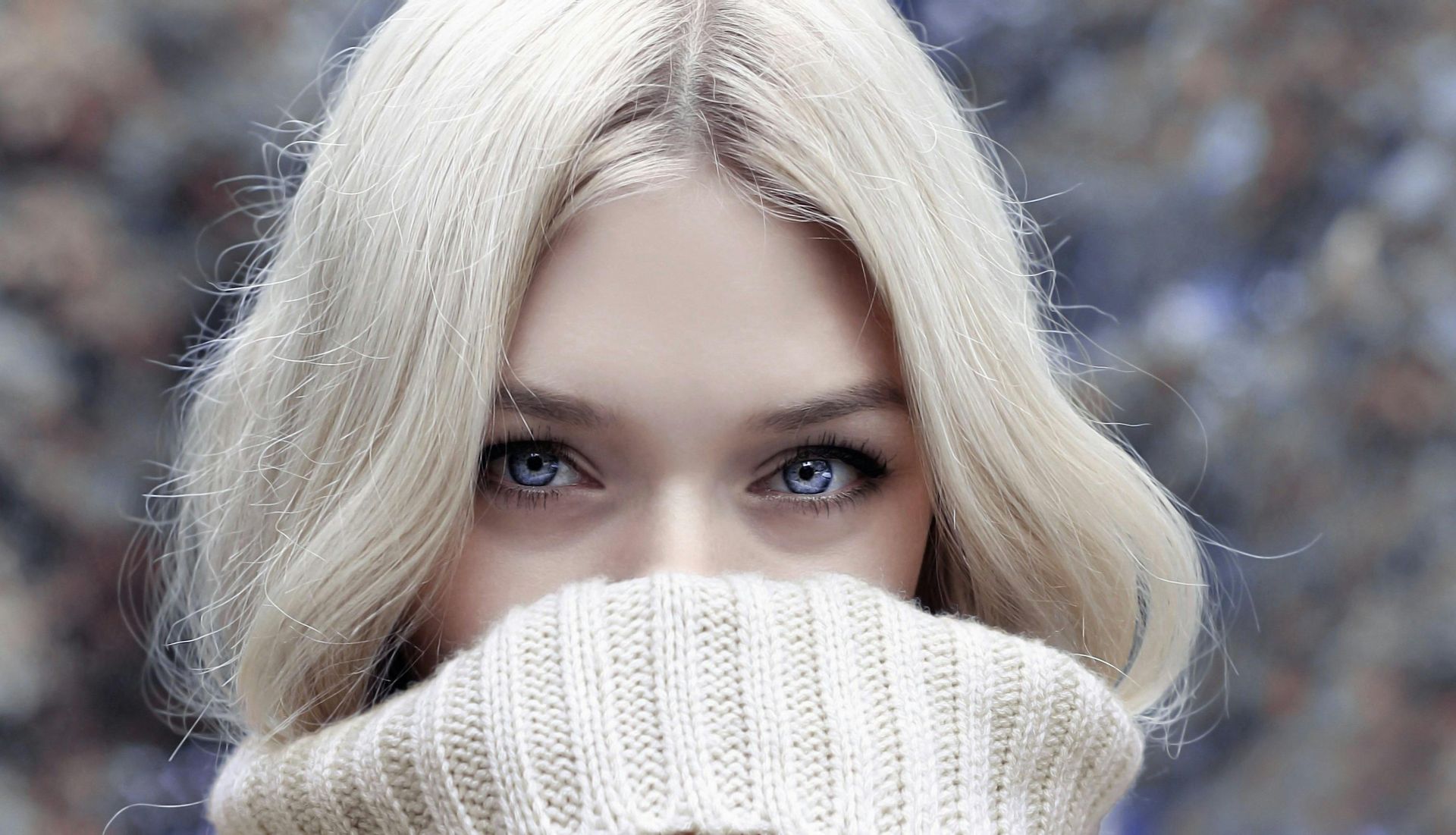 Woman with light blonde hair and blue eyes, wearing a cream-colored knit scarf.