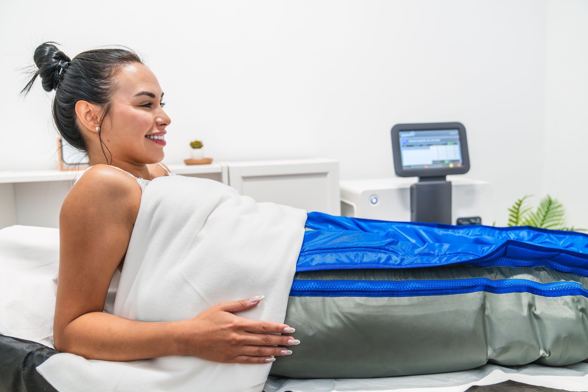 Donna sottoposta a trattamento di drenaggio linfatico, sorridente, coperta da un lenzuolo bianco, con apparecchio blu/grigio.