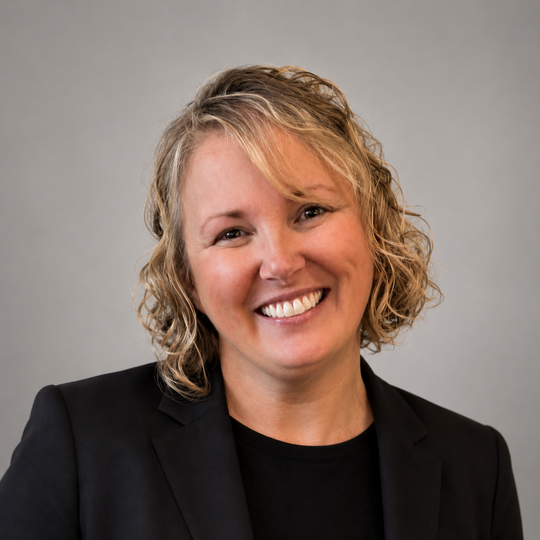Smiling woman in a black blazer against a gray background