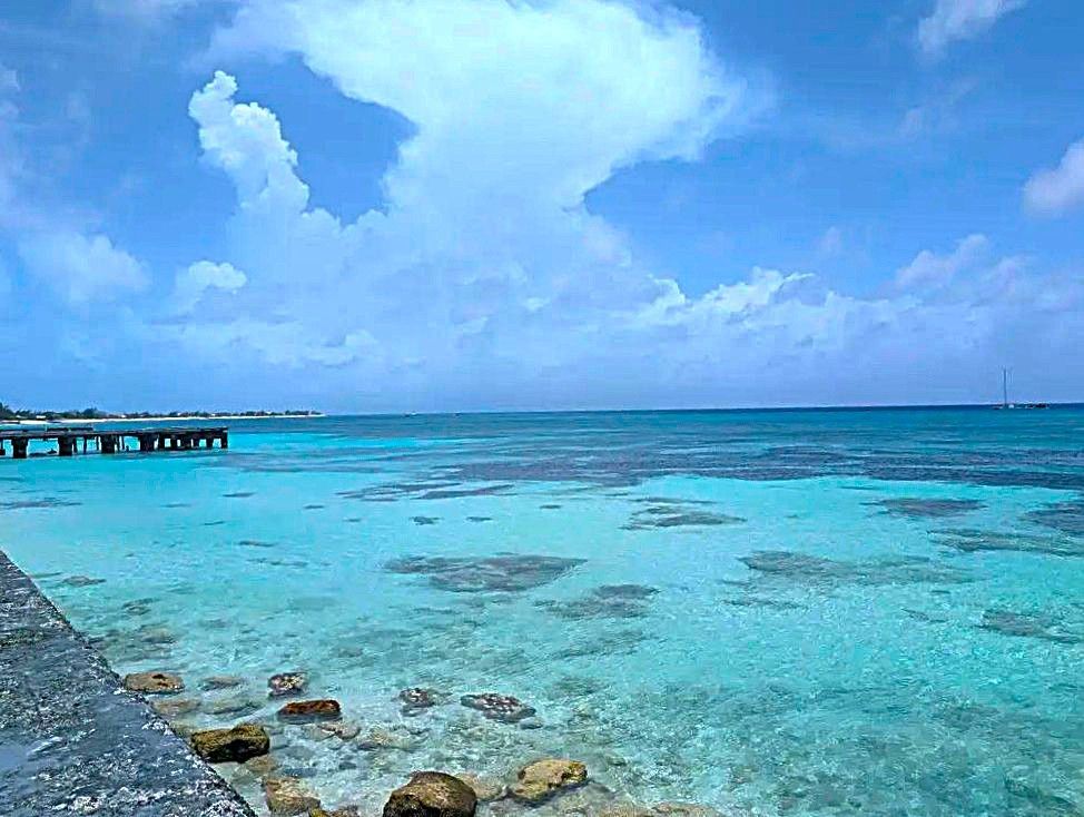 Tropical turquoise lagoon under a blue sky with clouds, rocky shore in foreground and a distant pier
