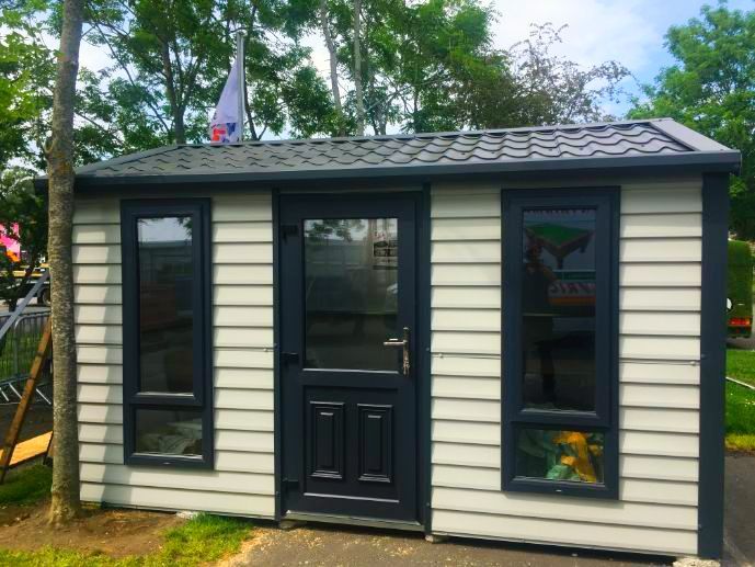 A small white and black shed with a roof and windows.