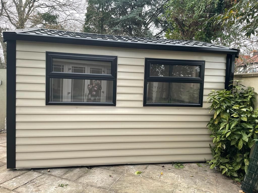 A small house with a roof and two windows in a backyard.