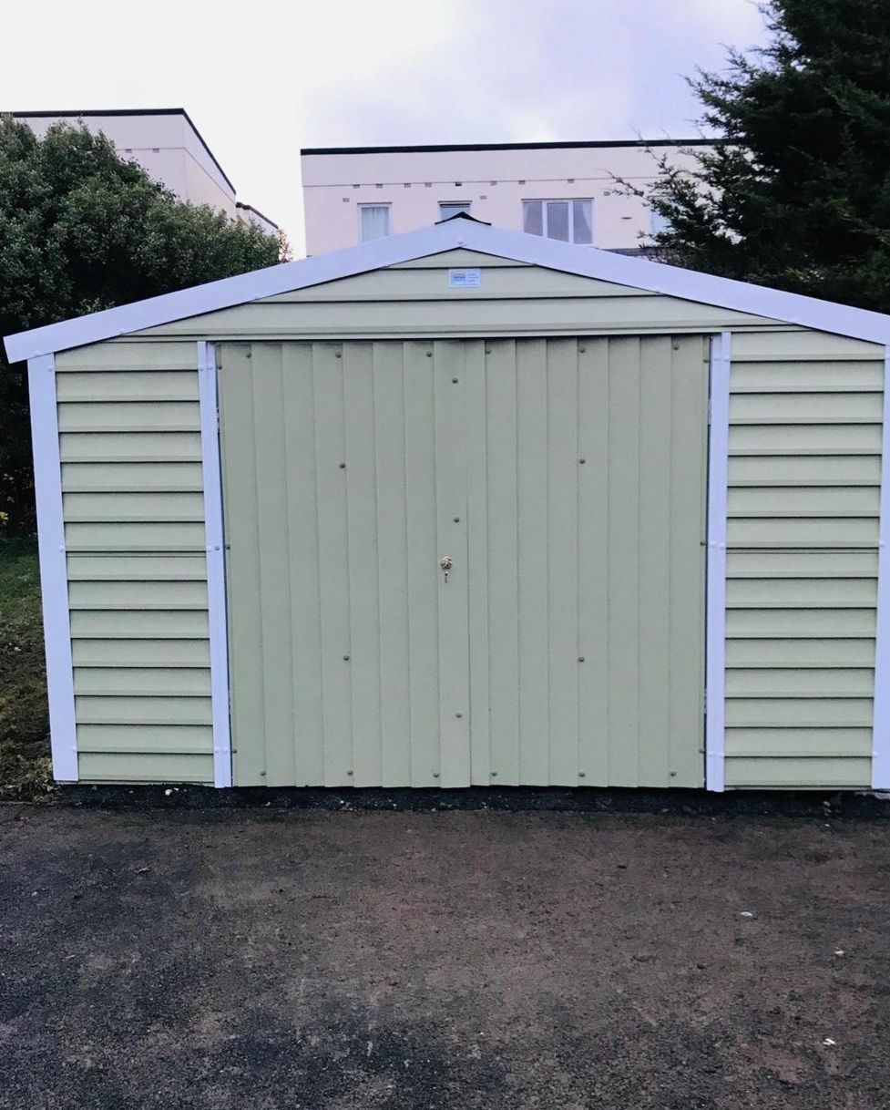 A green garage with a white trim sits in a driveway